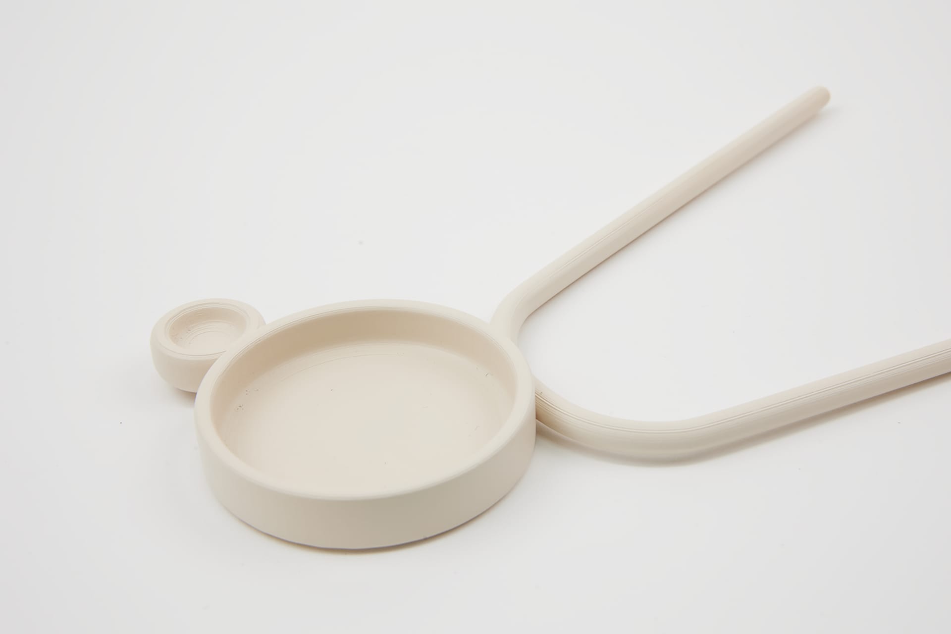 A beige sculptural object comprising of two circular shapes and a curved handle.