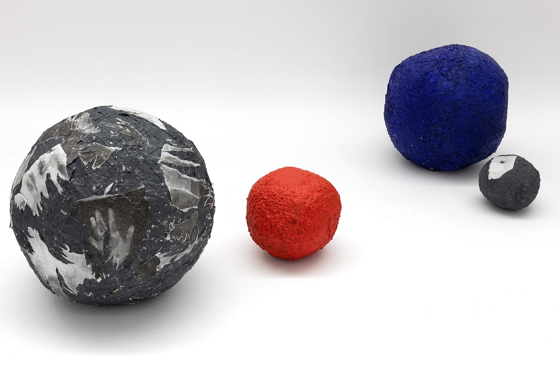 Group of four boulders of different sizes spread on the floor. One red, one blue and two with lithographs on their surface.