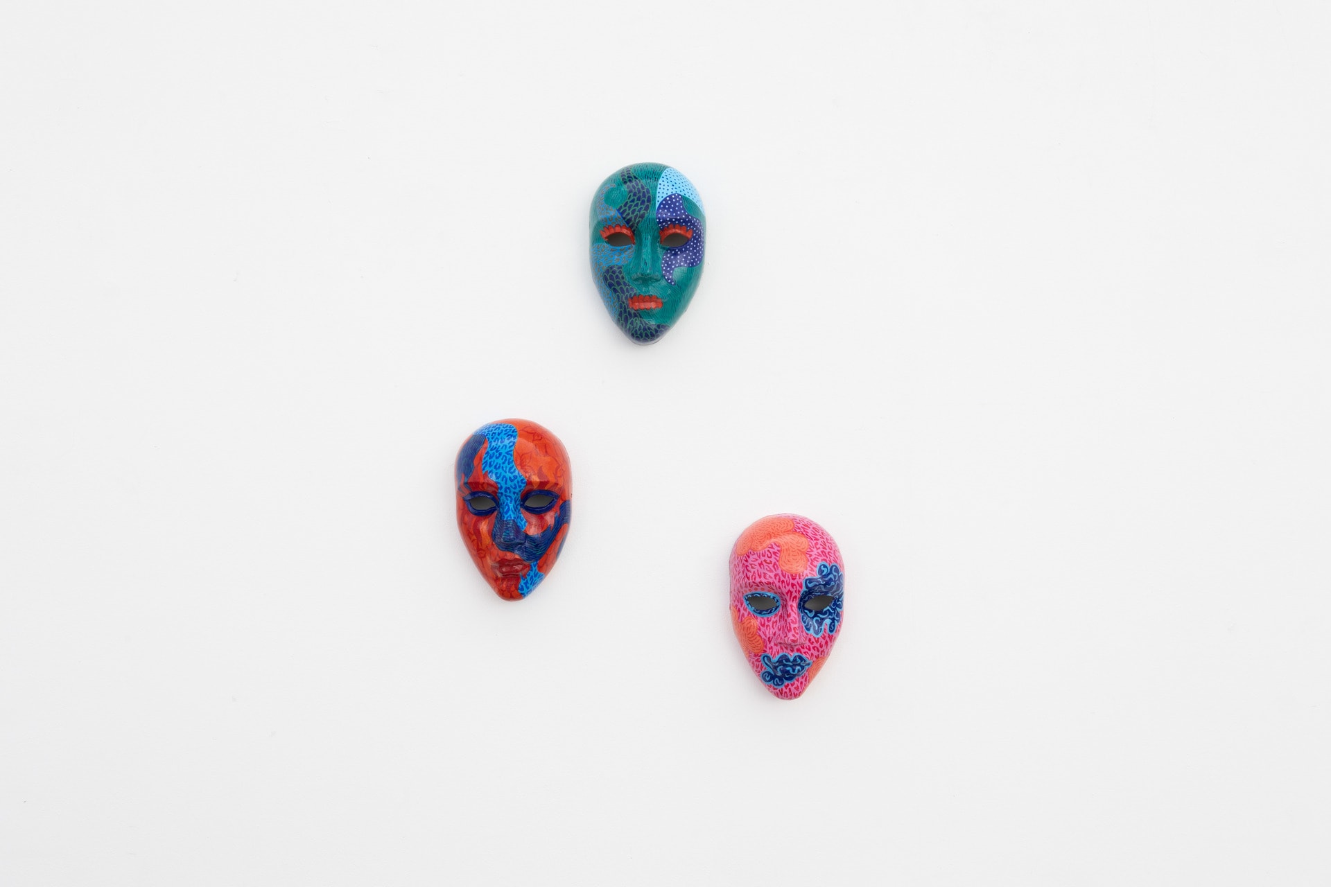 Three masks: Green, red and pink. Painted patterns and motifs.