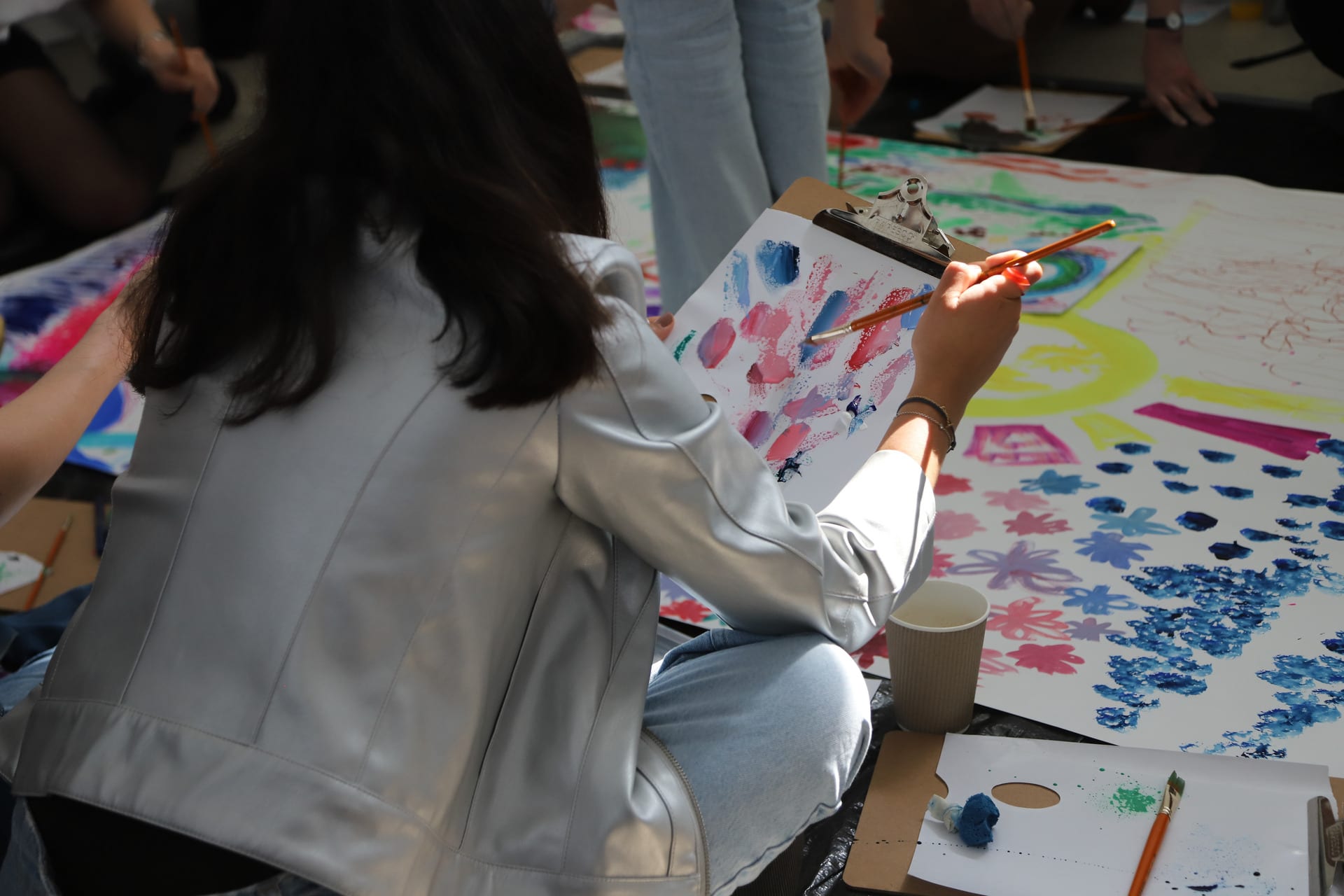 A woman in a silver jacket sits on the floor painting.