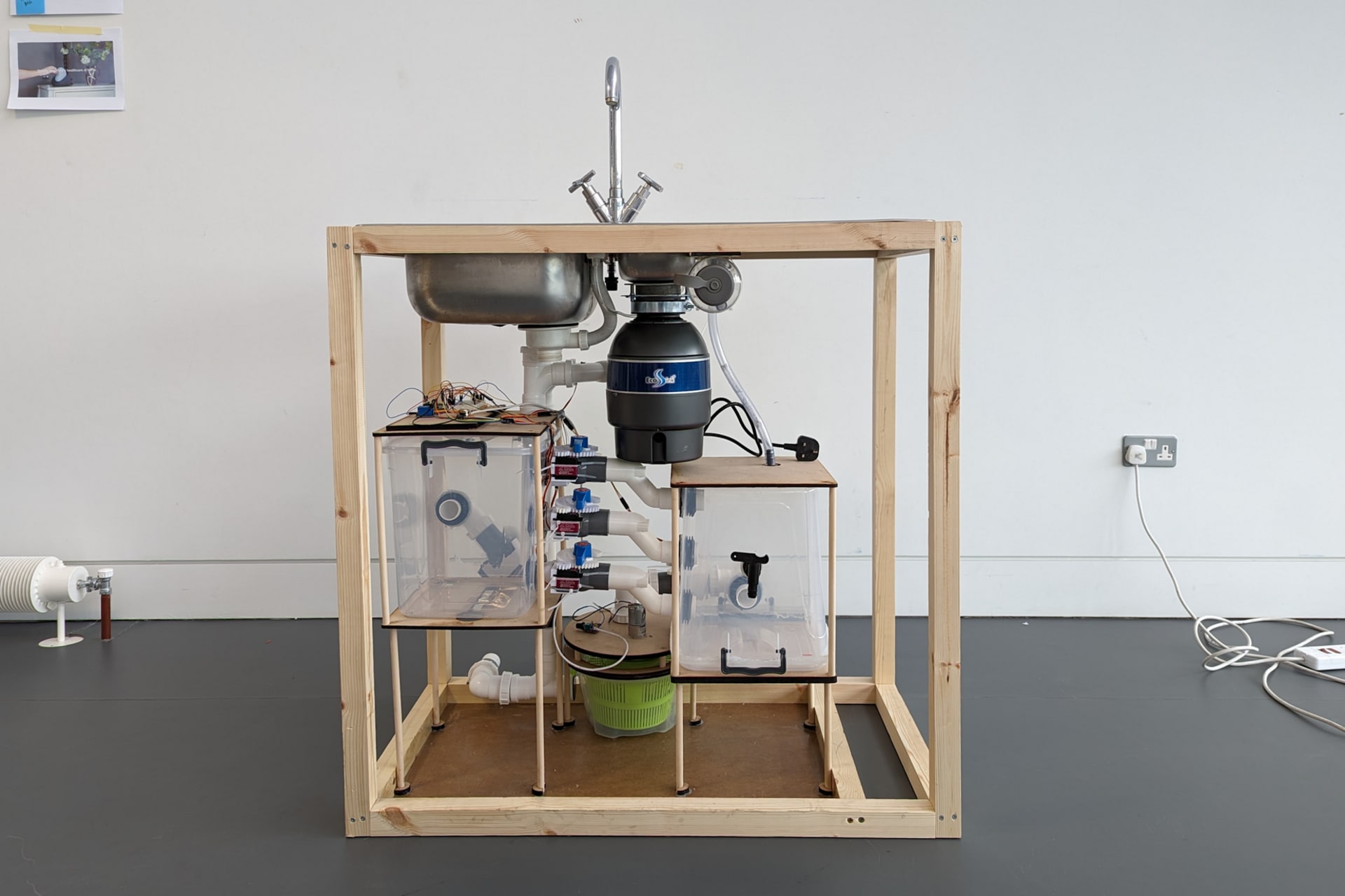 A prototype sink digester for biodegradable domestic waste constructed from timber and mdf, with plumbing components installed.