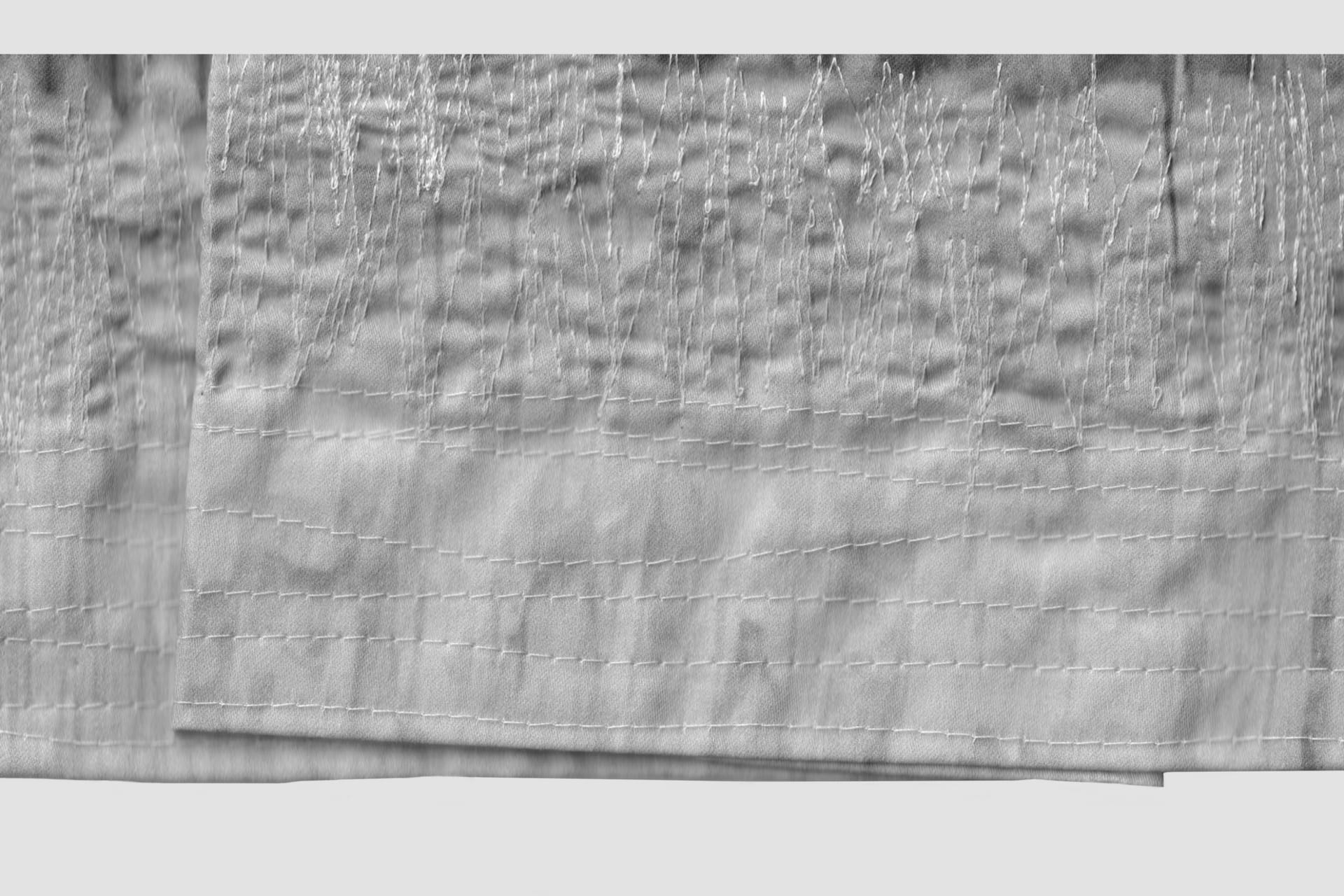 A close up of a scanned textile. The image is grey with multiple lines of embroidery, horizontal and vertical.