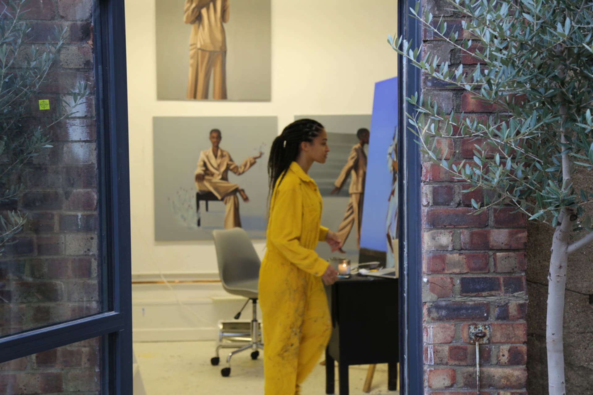 A woman in a yellow jumpsuit walks between paintings.