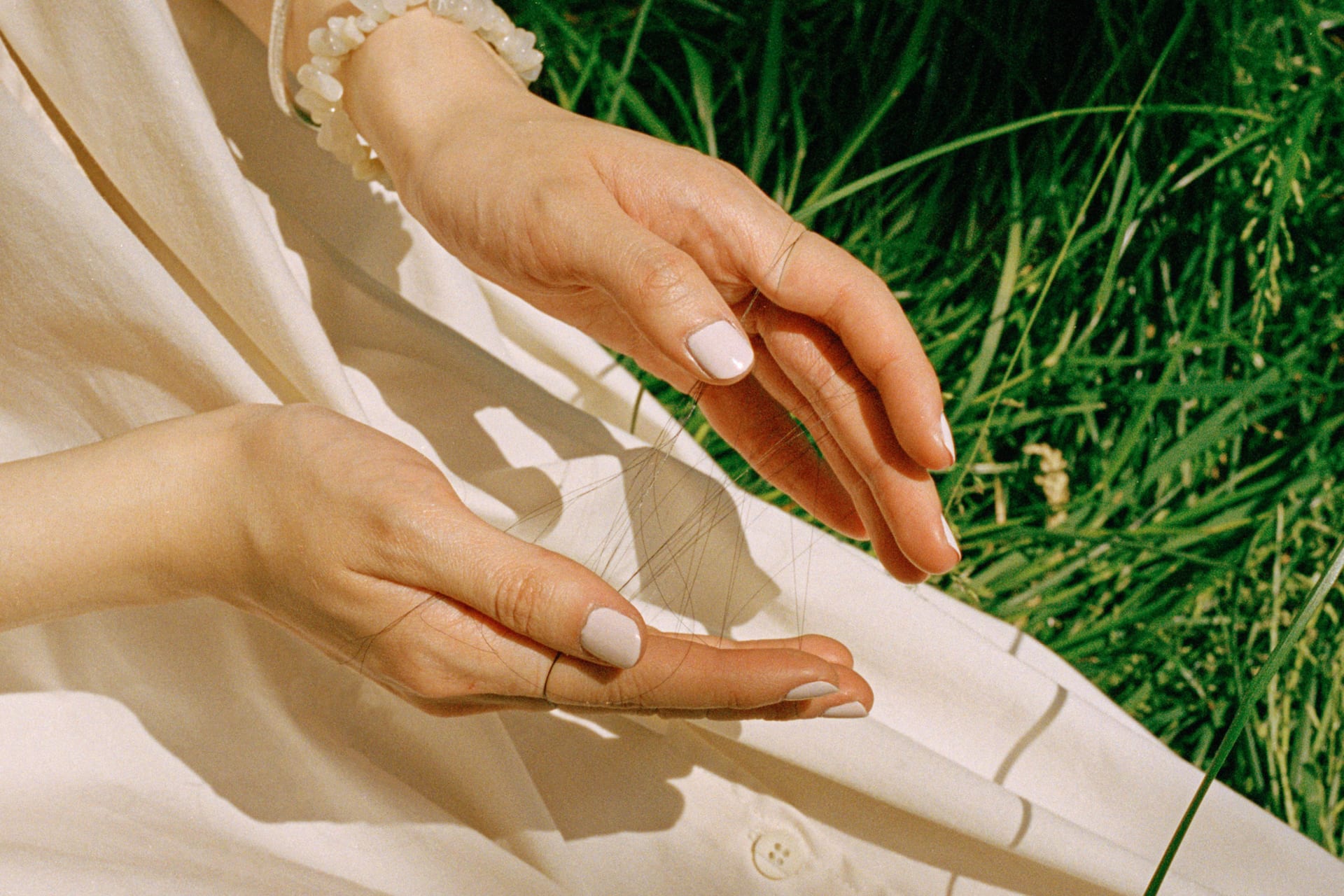Several strands of hair wound around the fingers of the girl in a white dress against a background of green grass.