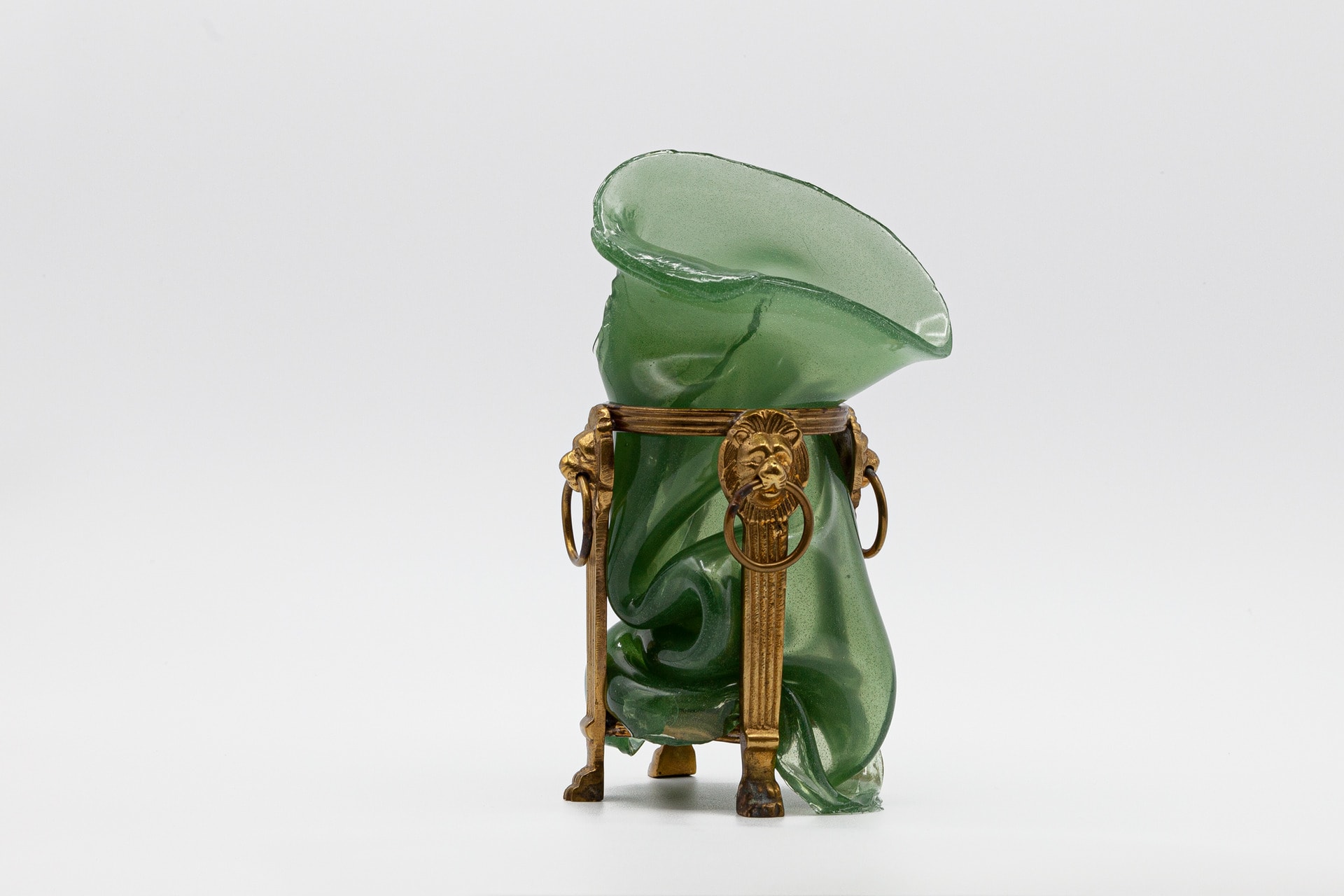 This image depicts a green vase melting down over an ornamental bronze base.
