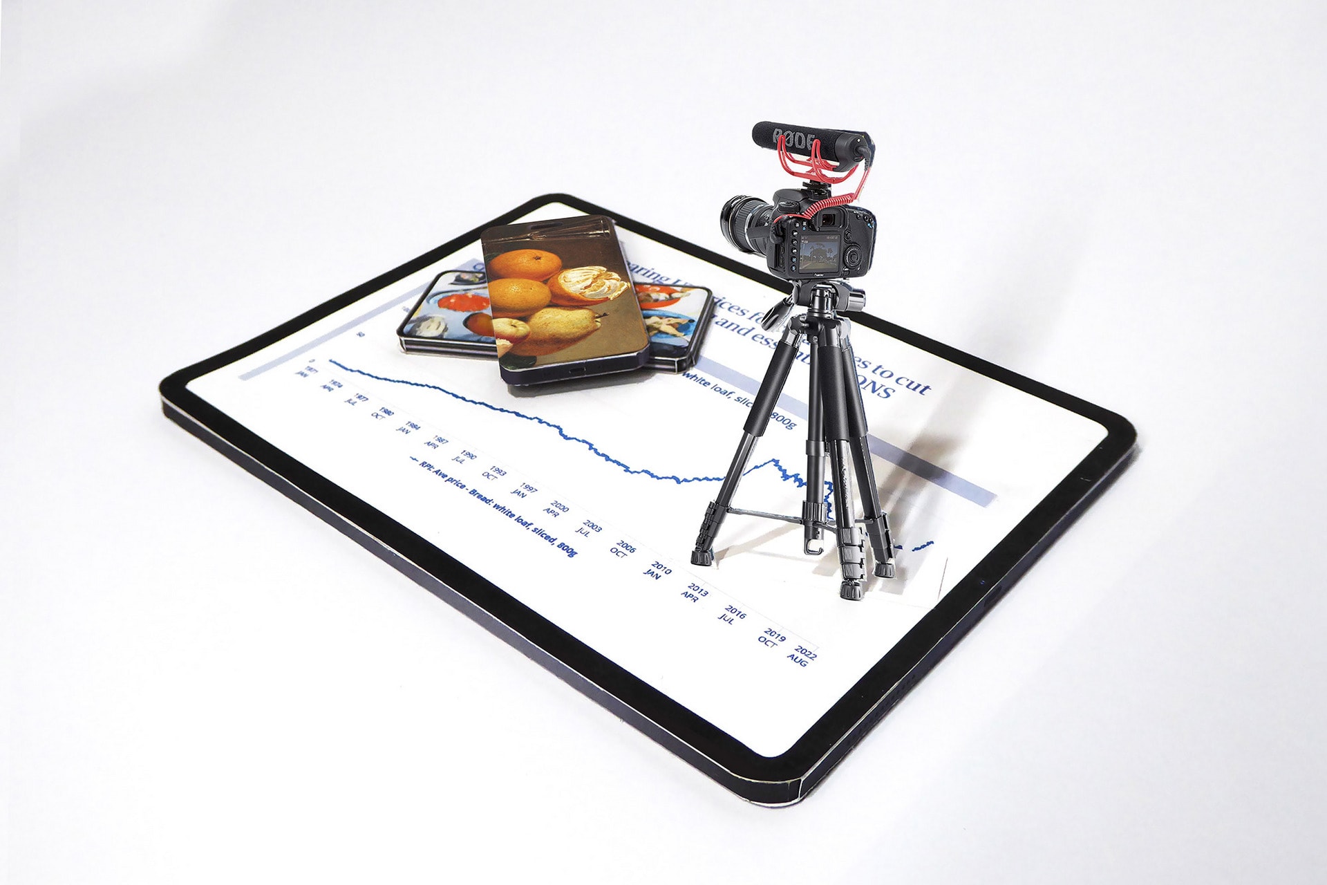 Printed card model of an iPad, with smaller models of mobile phones and a camera on a tripod.