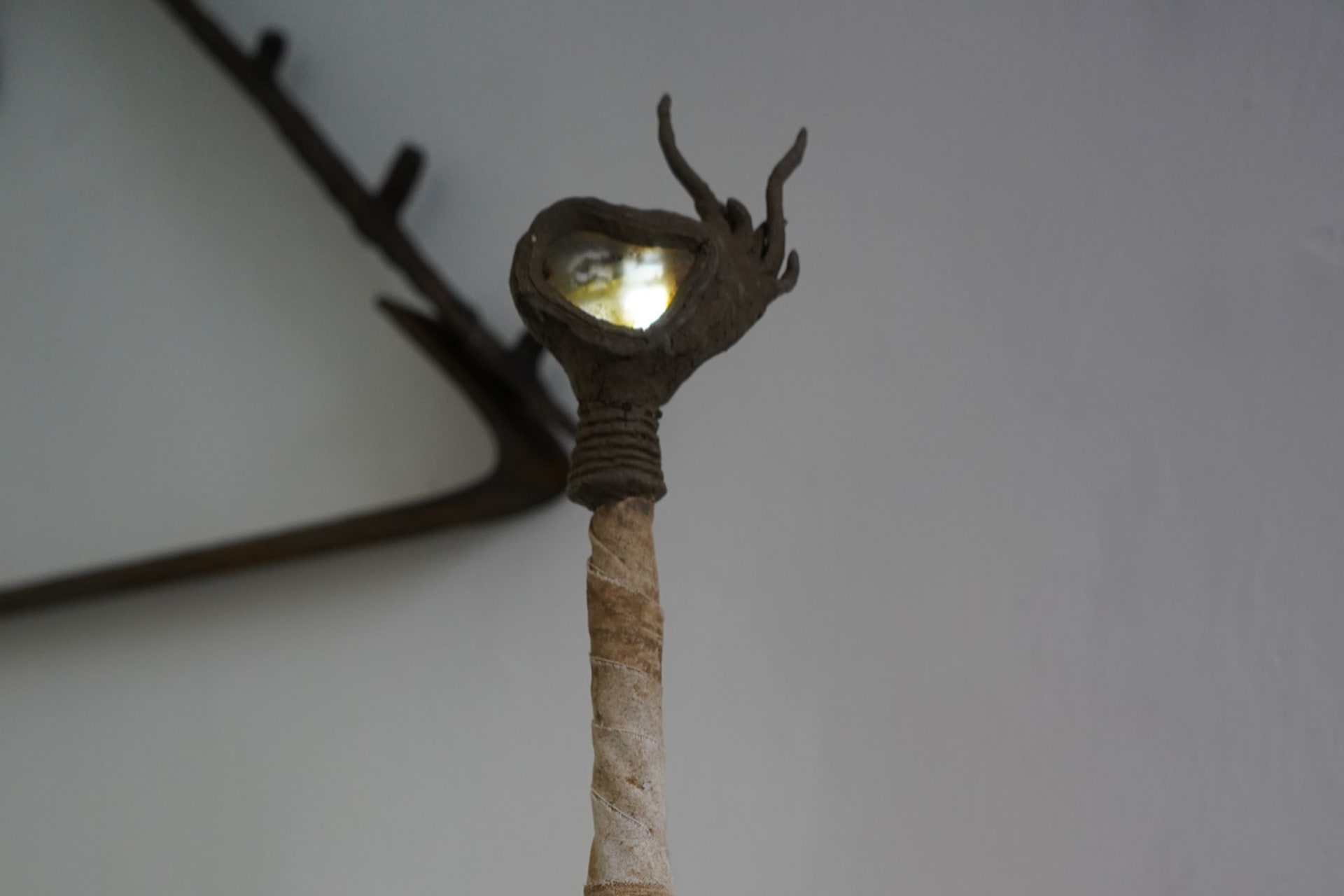 A cloth covered column with a spiny clay glob at the top. Embedded in this is a piece of amber, lit from behind, showing a cross