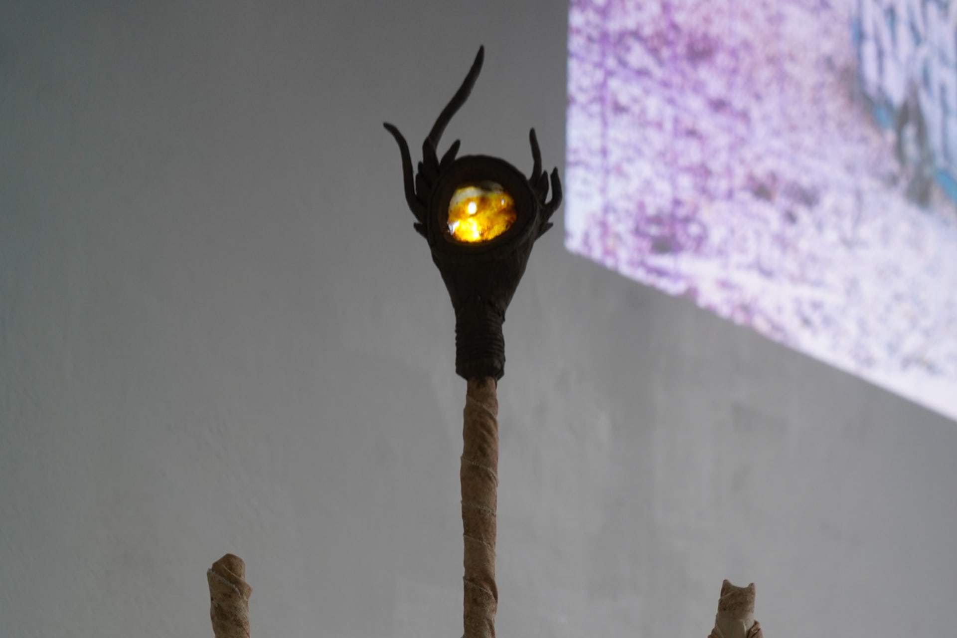 A cloth covered column with a spiny clay glob at the top. Embedded in this is a piece of amber, lit from behind, showing a cross