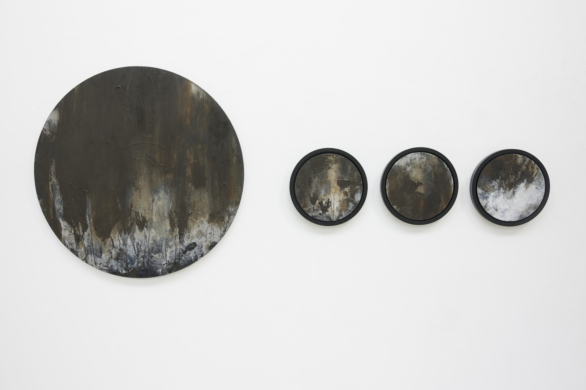 Four abstract circular canvases of earthy tones. One is much larger and three are smaller in black frames.