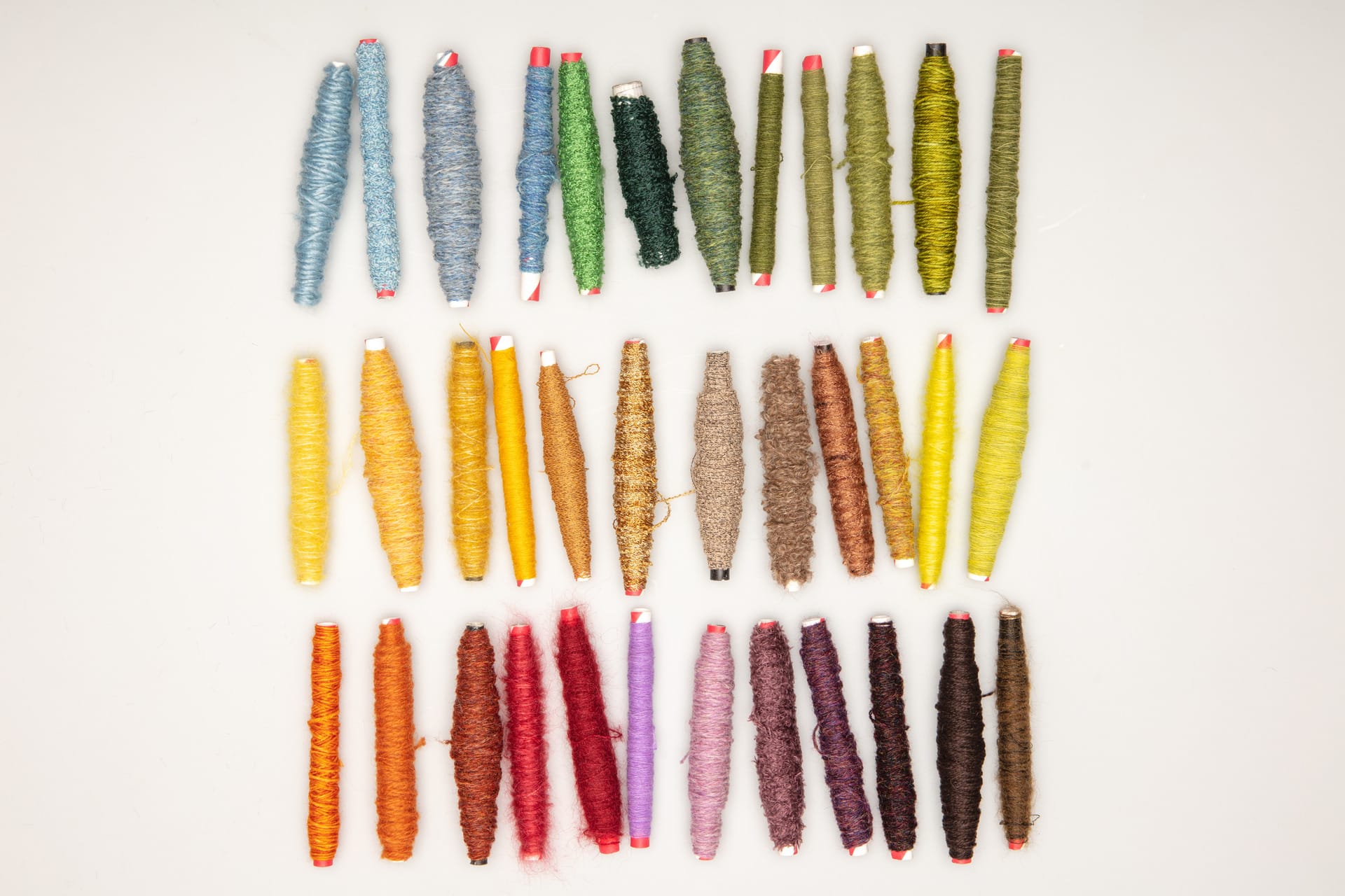 3 rows of bobbins are aligned showing different yarns in a variety of autumnal colours, against a white background