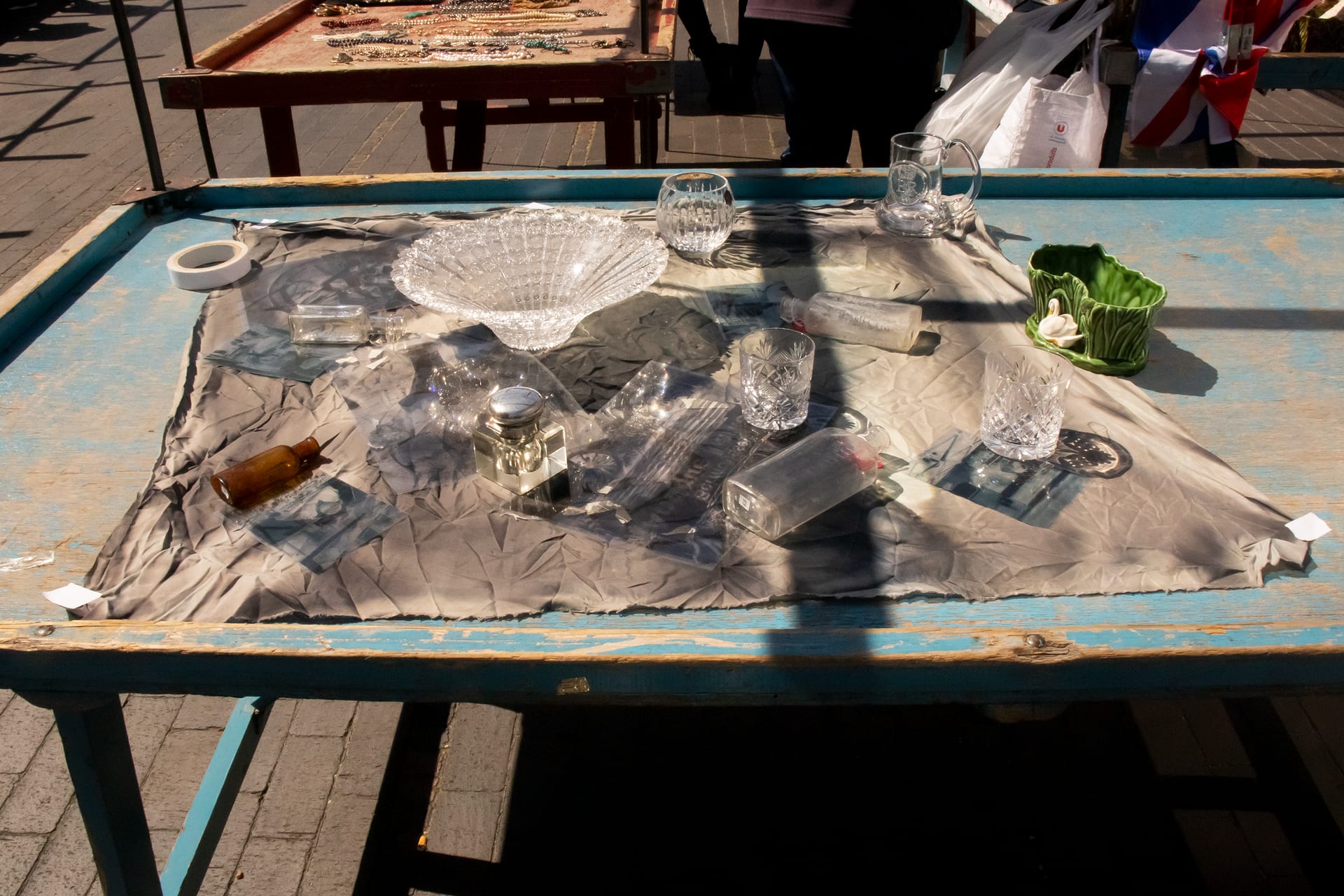 a piece of material sits atop a market stall, there are glass objects on top of the material, it is being exposed by the sun