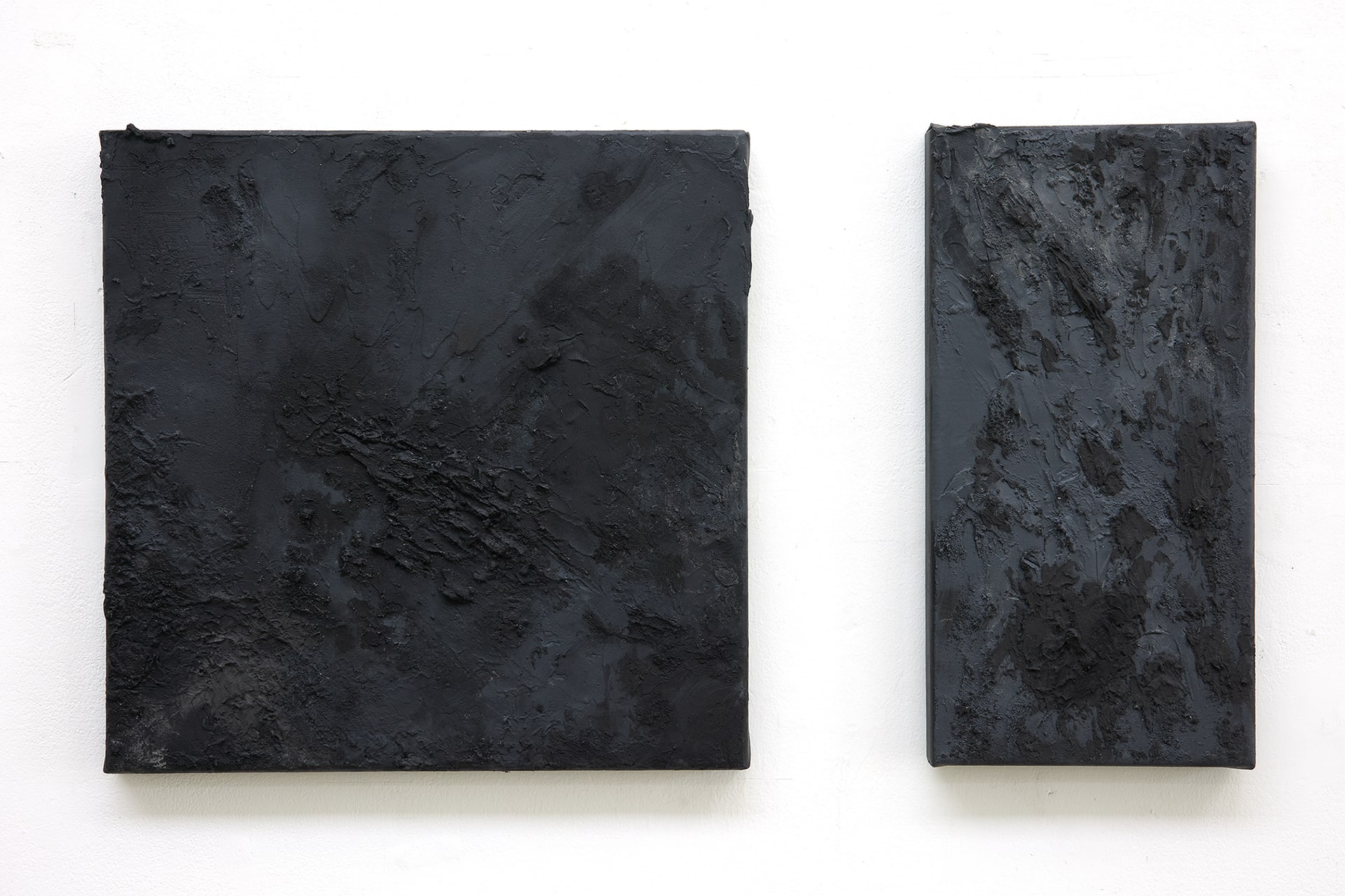 Two dark grey canvases with black textured surfaces. One is square and one is rectangular.