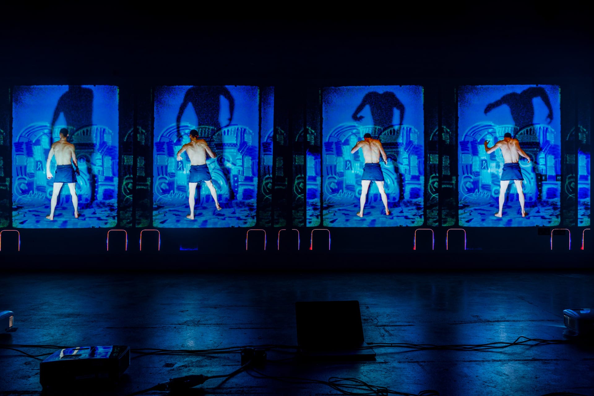 video installation showing a male dancer on a blue spray painted backdrop in different positions