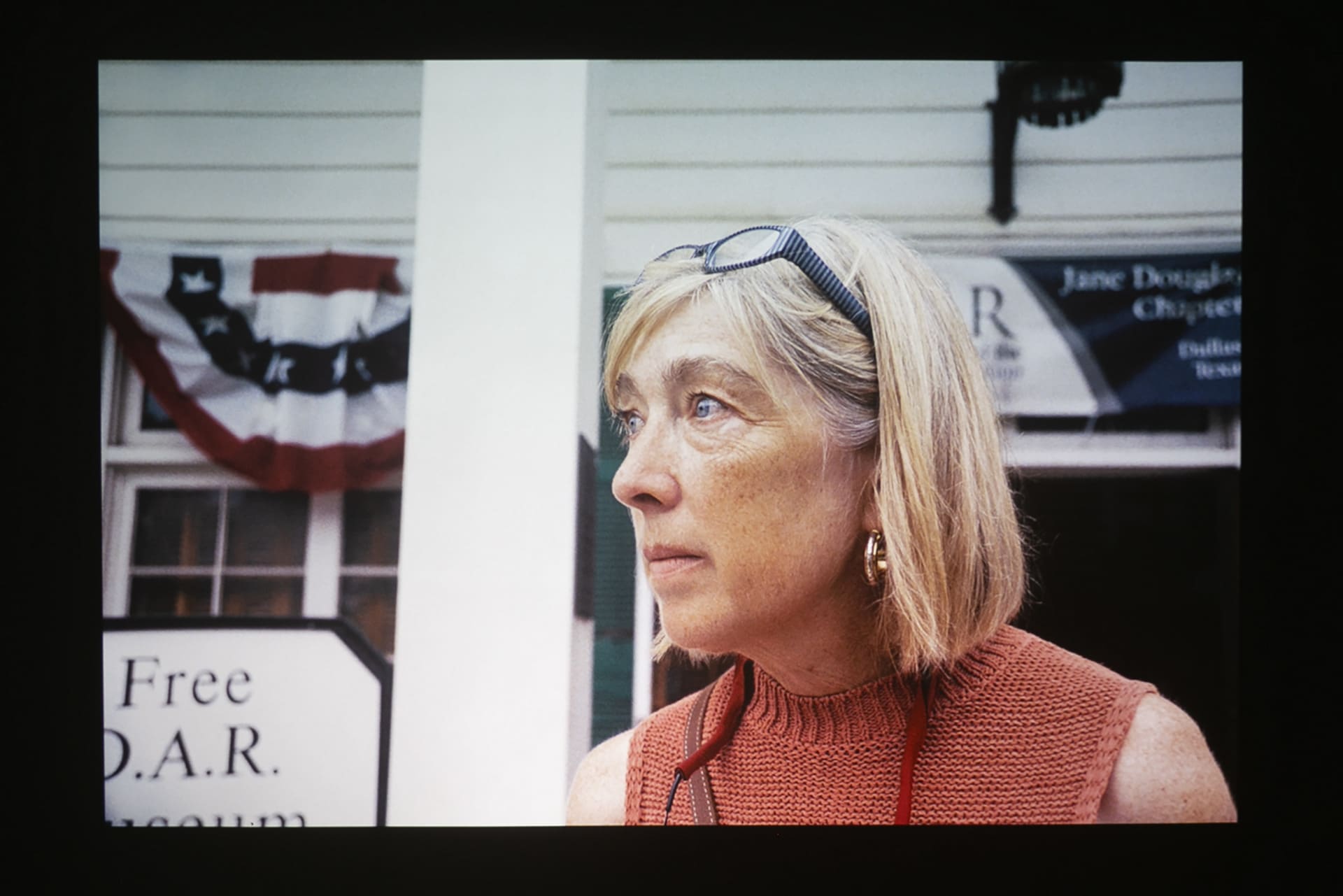 Woman in color looking away from the camera. Behind her is american flag and signages.
