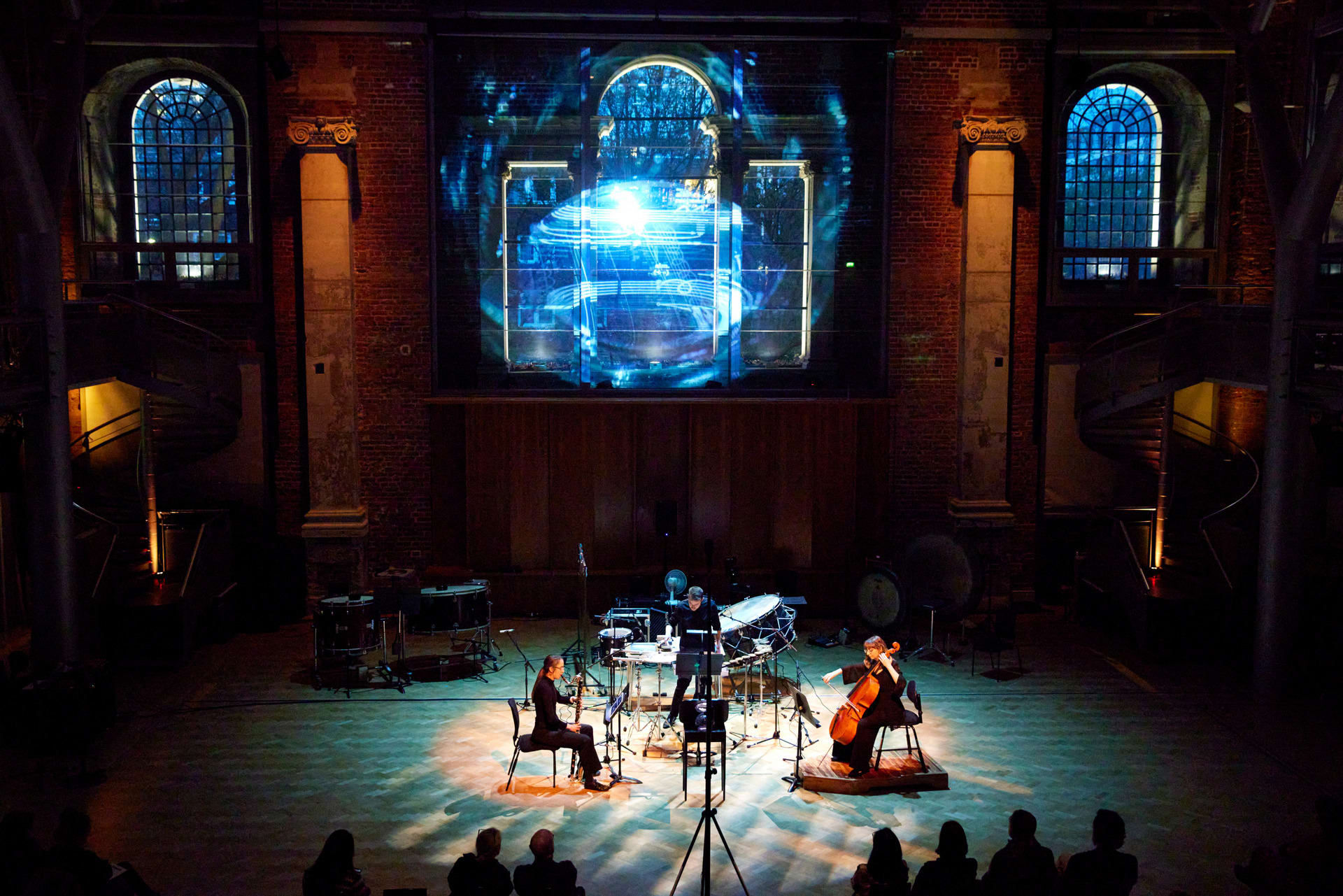 A chamber trio are arranged around a crystal-ball sculpture. A projection hovers above them, reflected off the arch windows. 