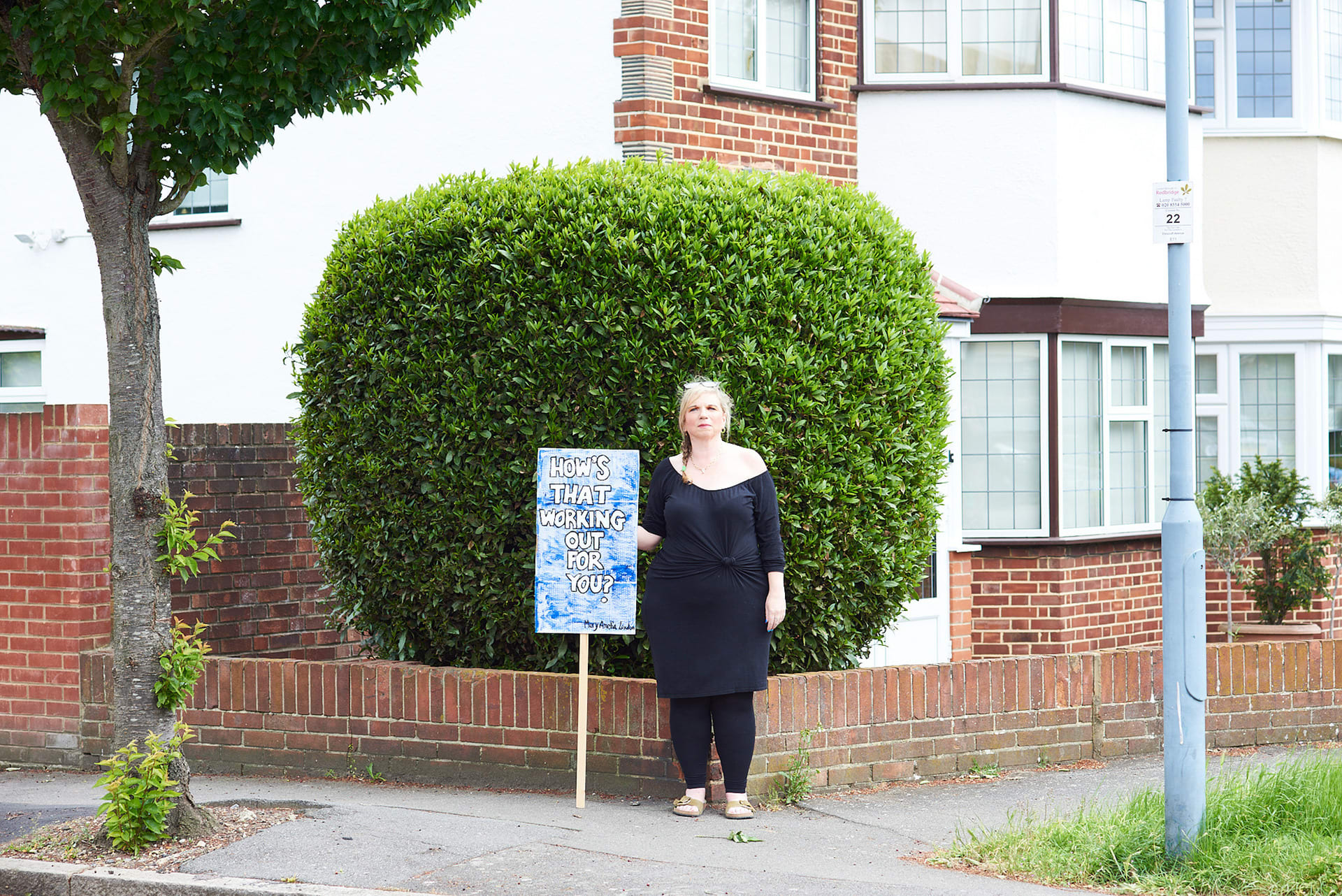 Mary Amelia London stands holding a sign that says: 'How's that working out for you?'