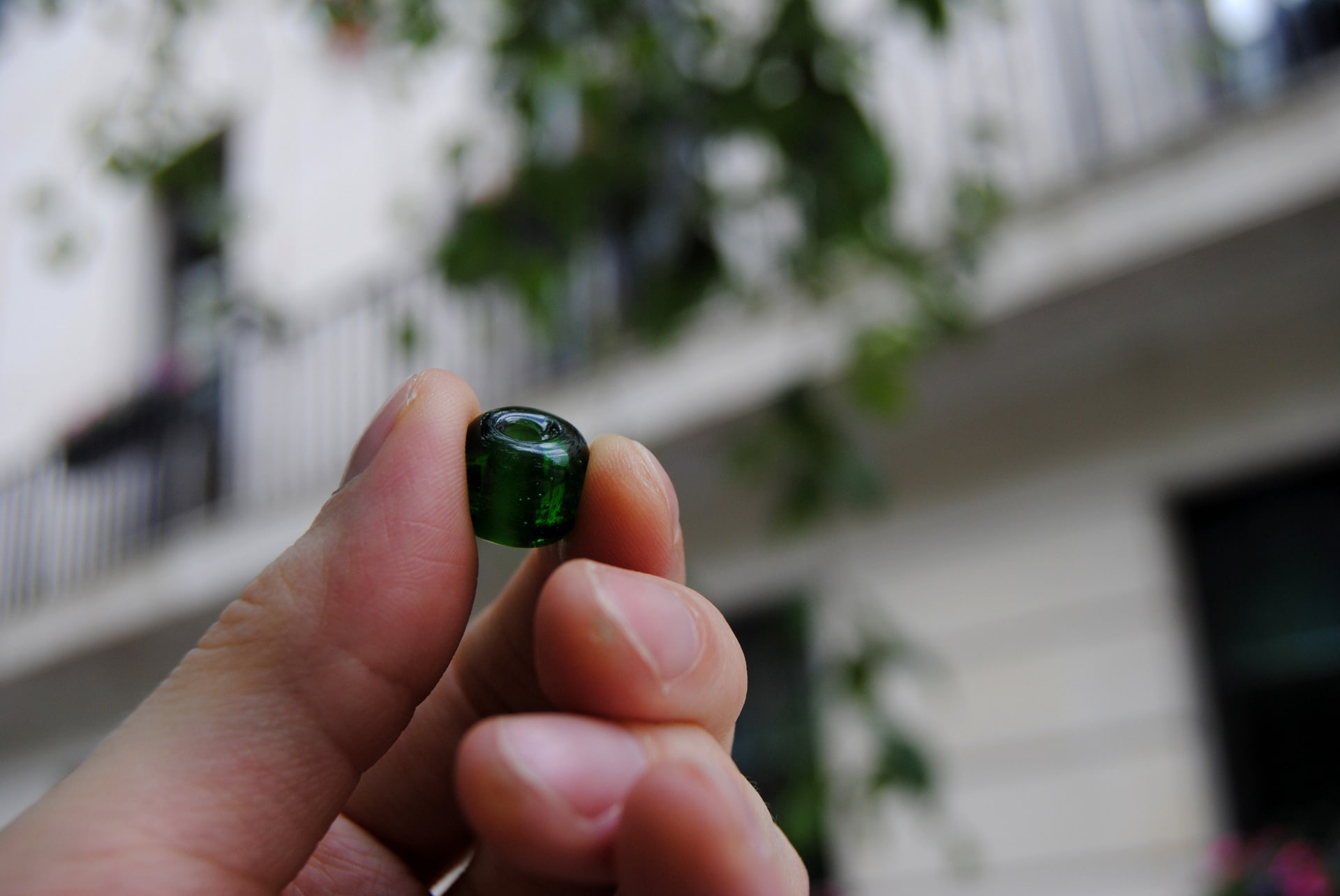 close up of hand holding green glass bead with trees in the background