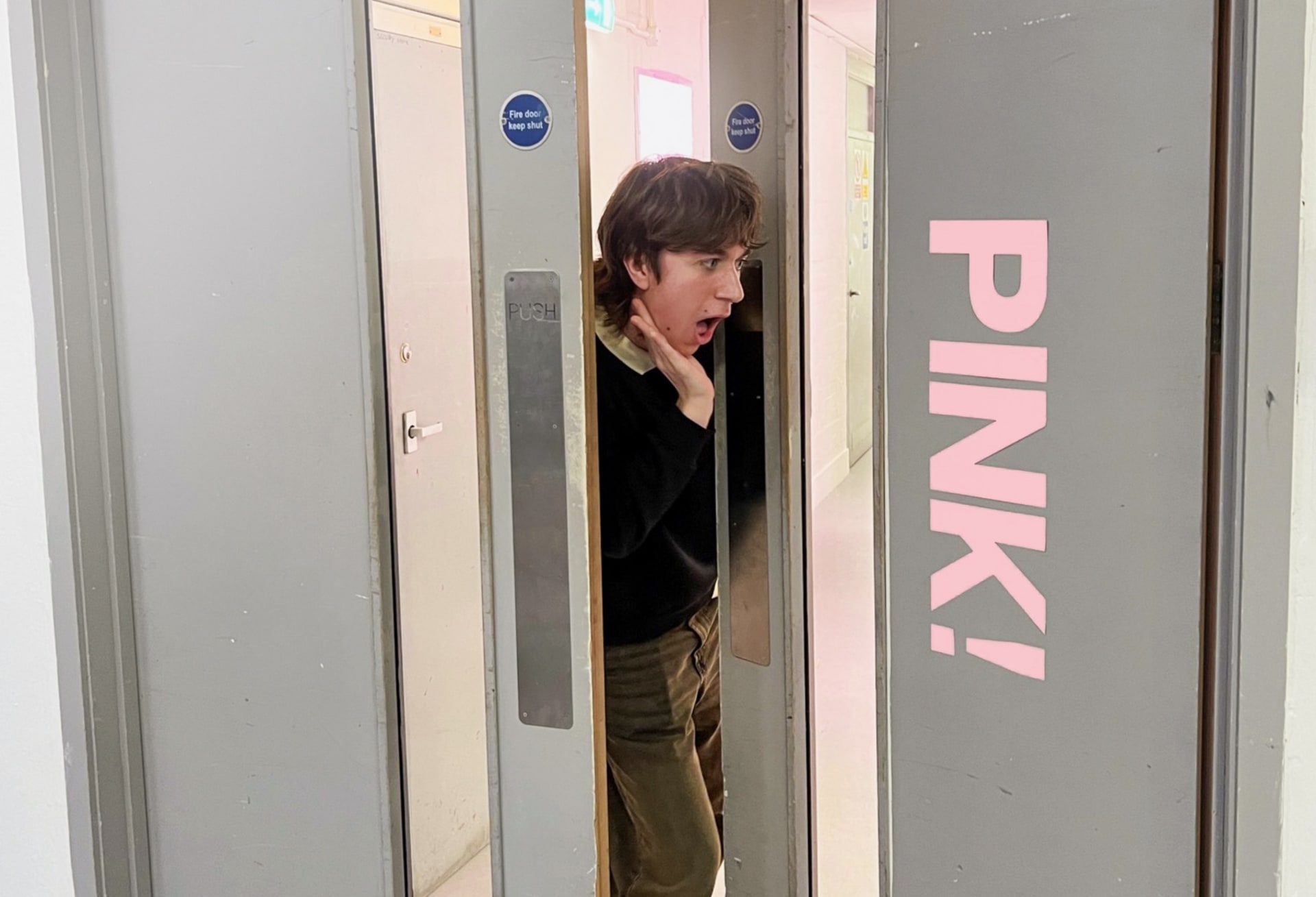 A handsome young man opening a door with a huge "PINK" text on it. He looks surprised and excited about the text.