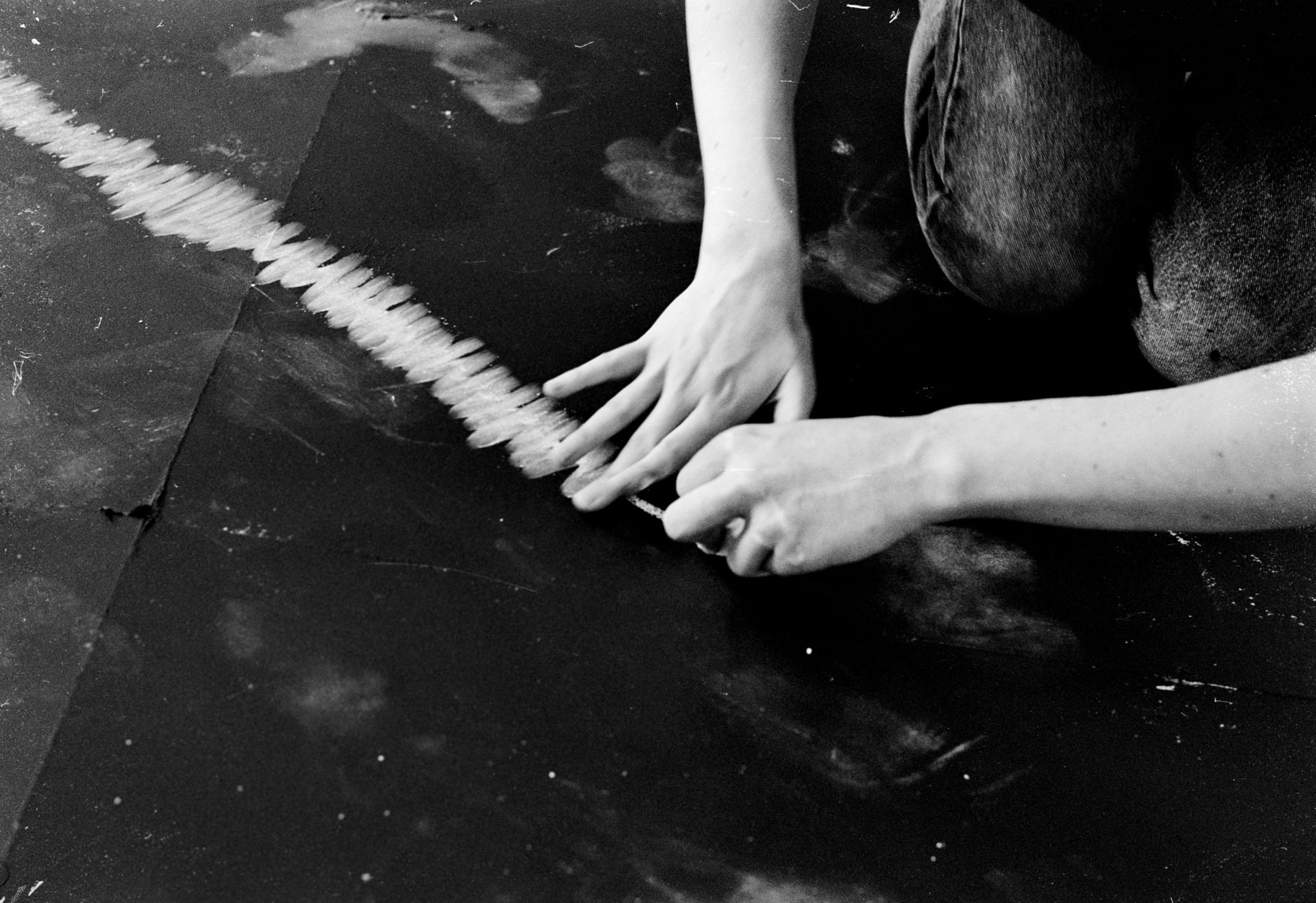 Image of hands making marks on a blackboard with chalk, while one had draw with the chalk the other follows and wipes it away. 