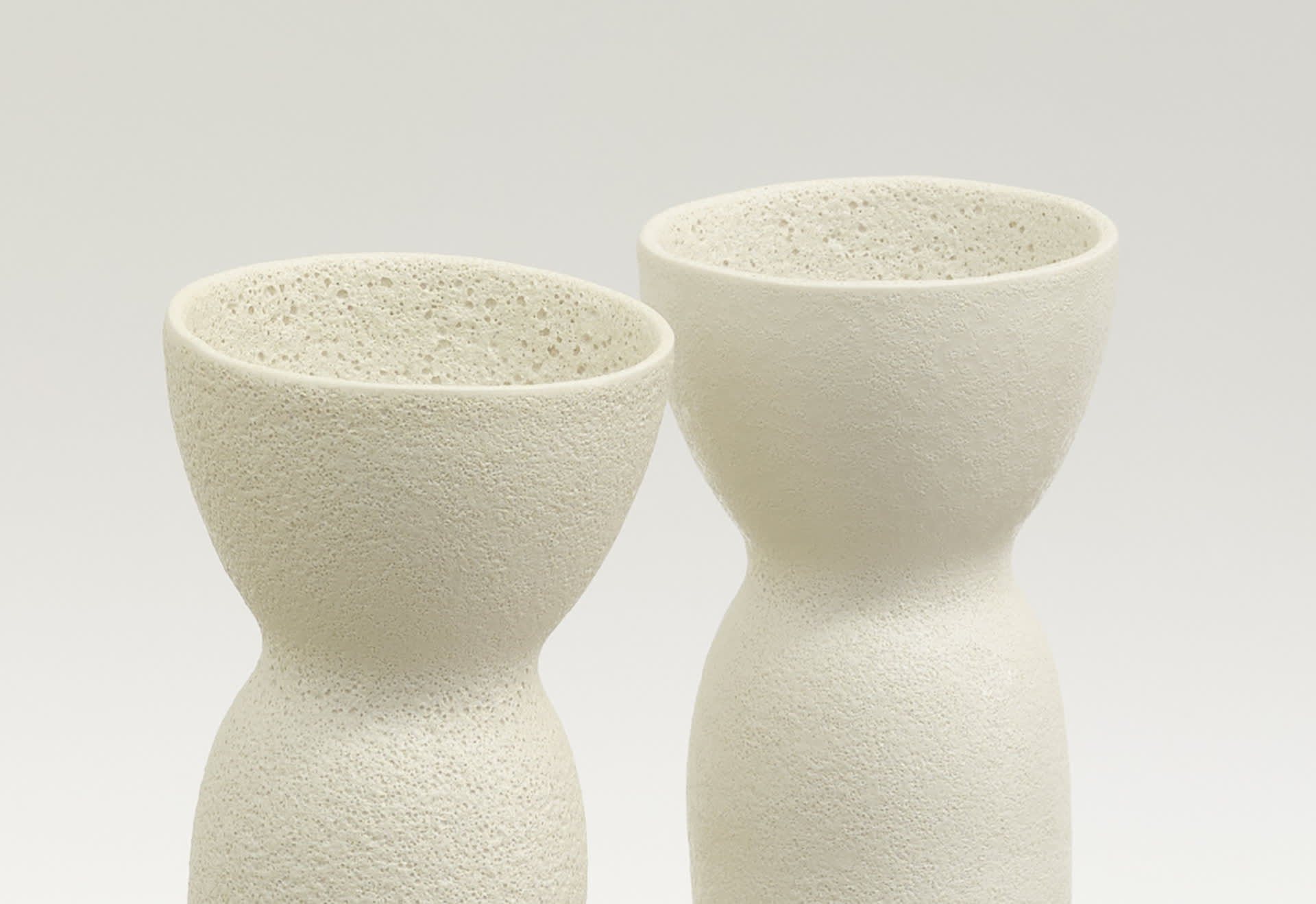 two matching vessels that lean slightly towards each other. they have a textures crater like glazed surface