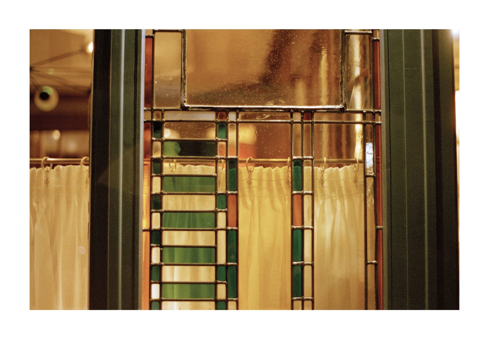 A Photograph stained glass window, with green, yellow and orange colours. theres a curtain that flows down half way of image 