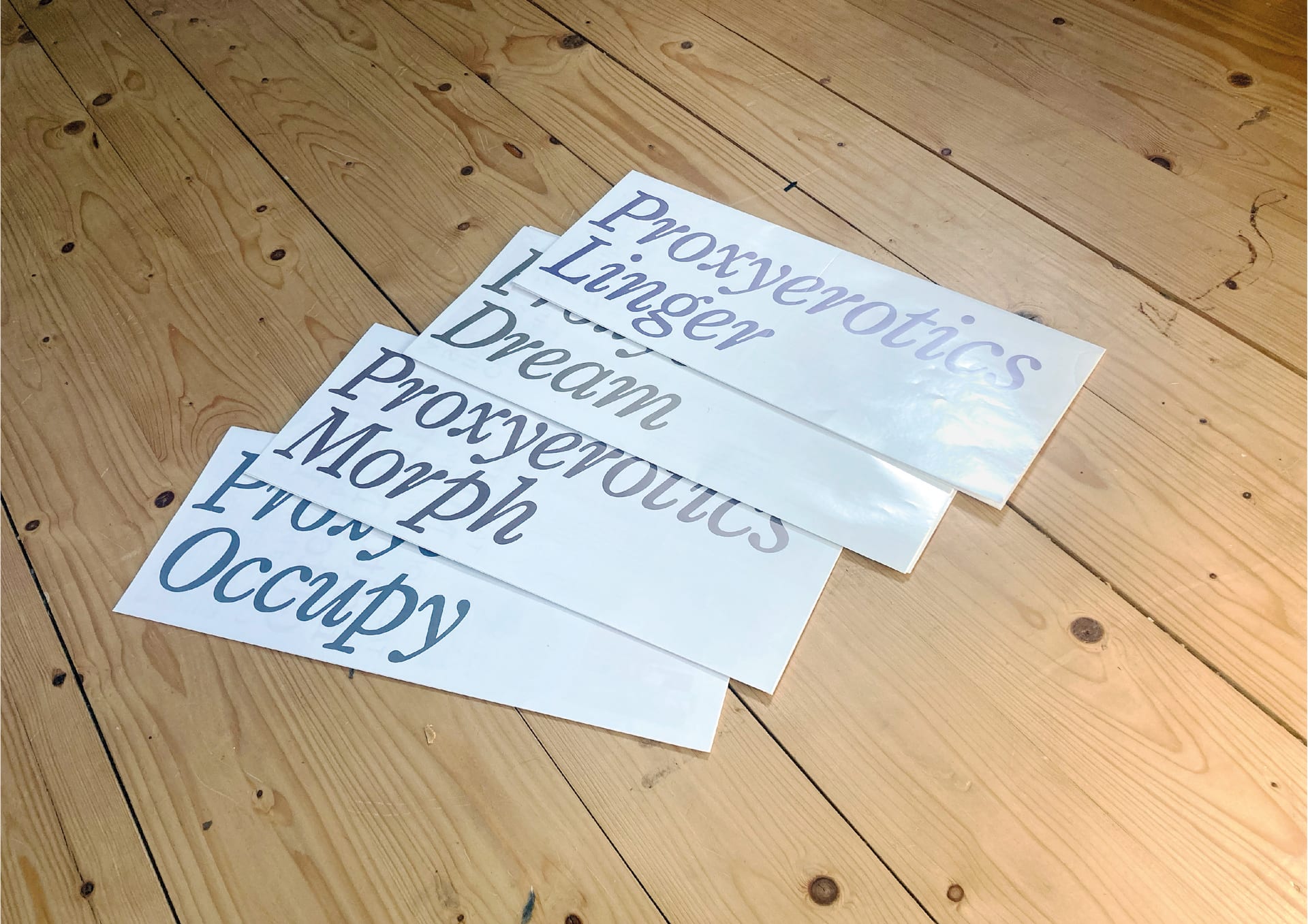 ARC: Proxyerotics, a series of 4 largescale foldable publications, fanned out on a wooden floor.