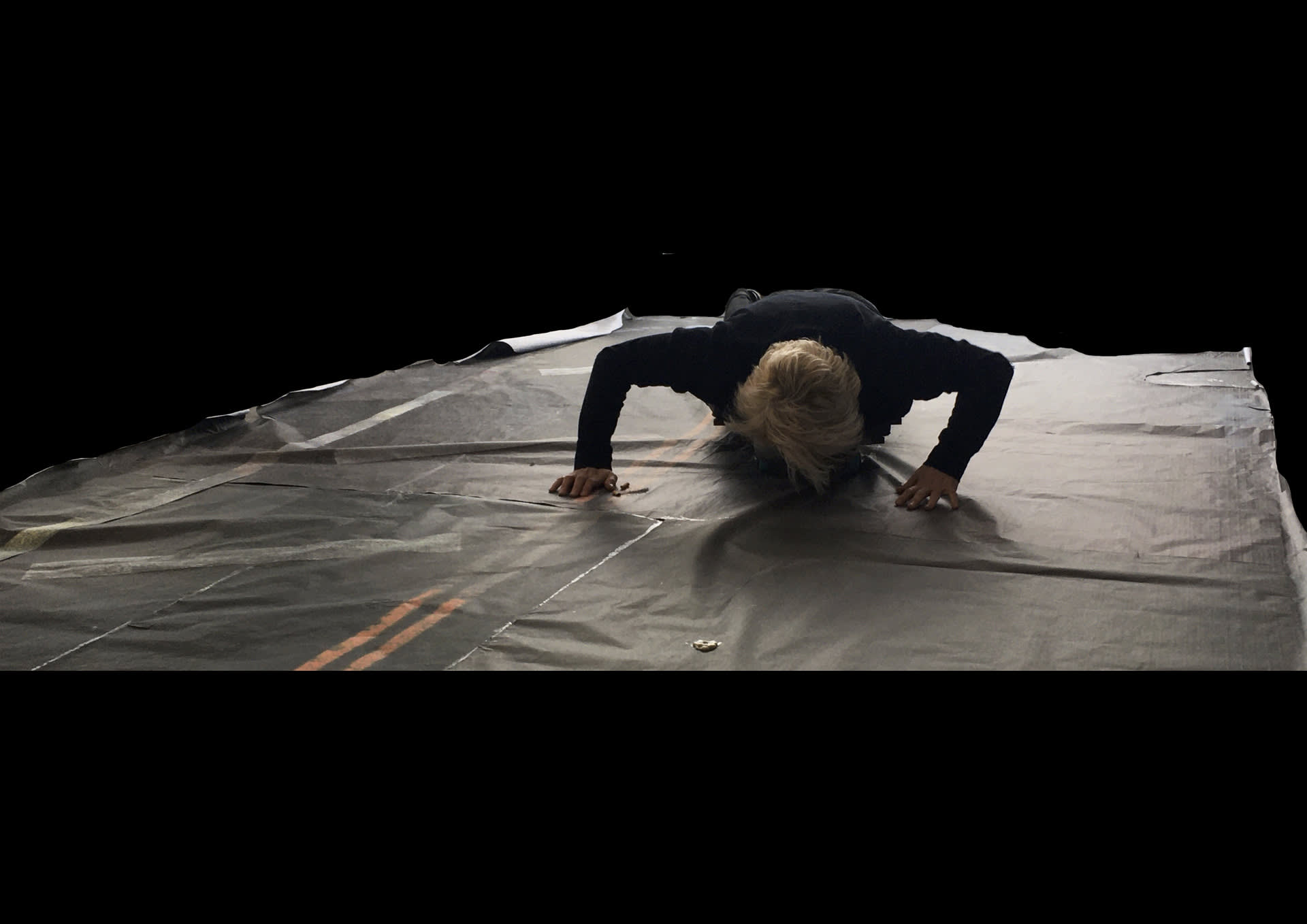 a white woman riding a skateboard on her belly sniffing at cigarettes on a printed paper pavement 