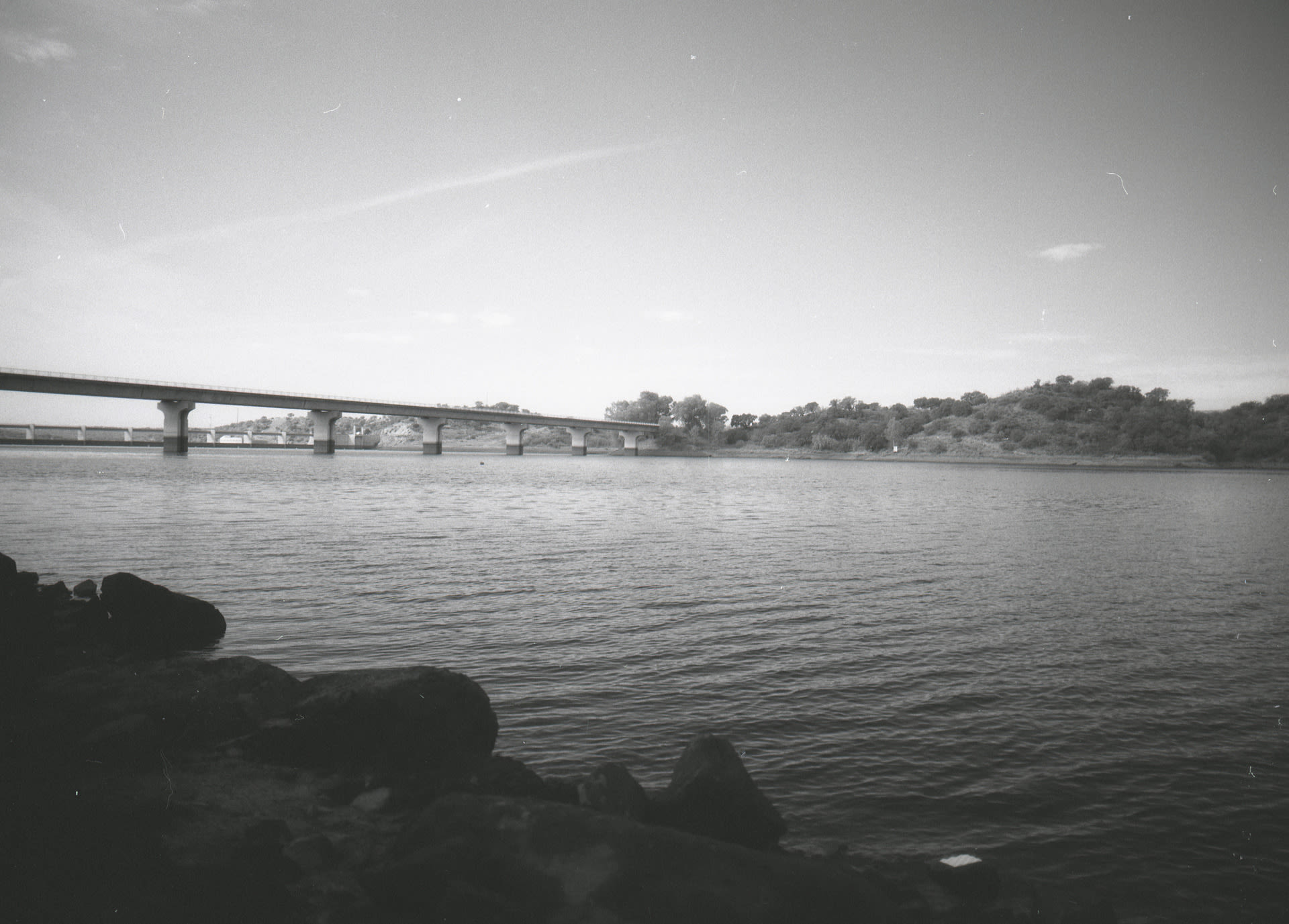 tile on rocks in forground. mid frame calm river waterbody. concrete bridge crossing river