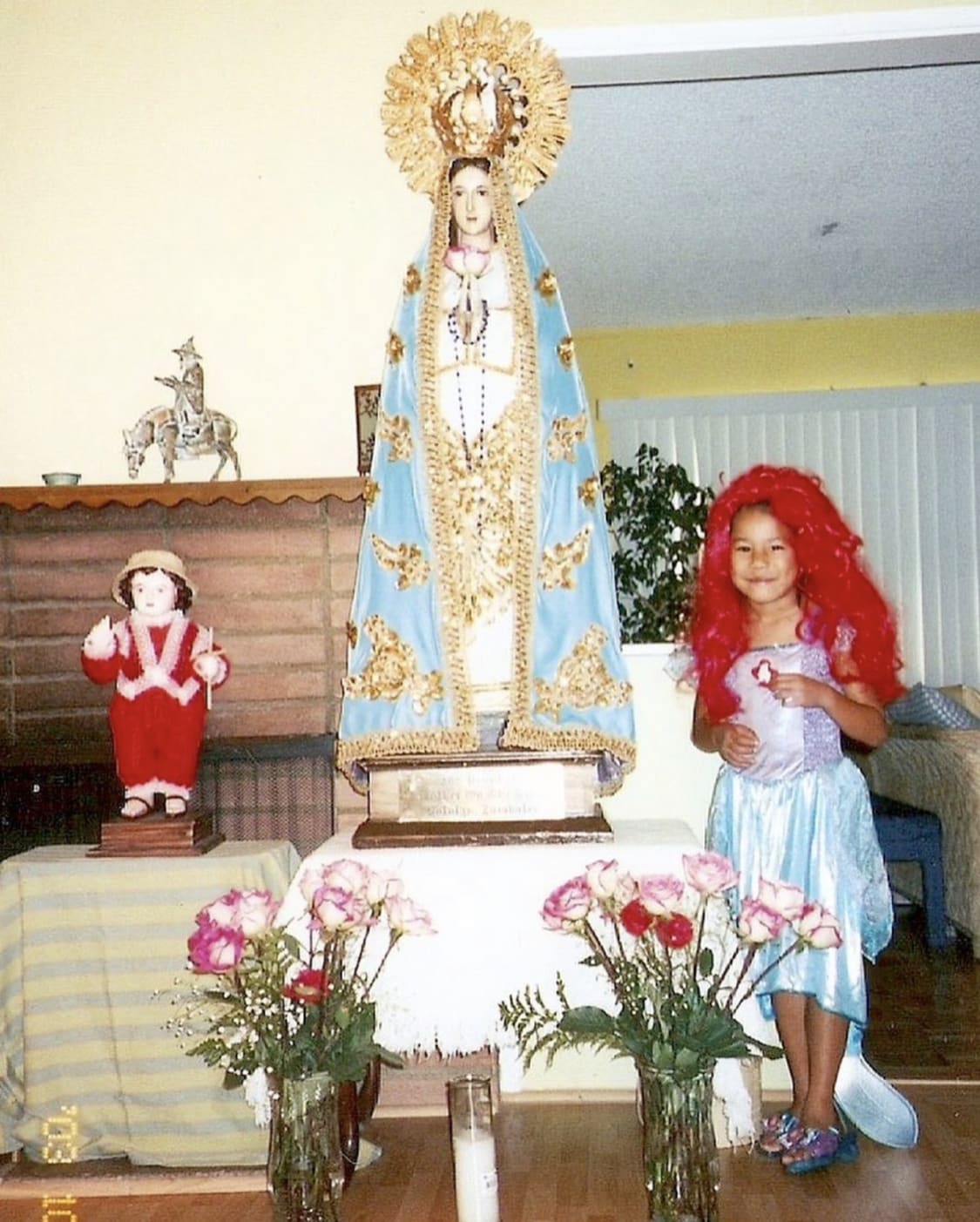 The image presents a young Crysta dressed up as The Little Mermaid next to the Virgin Mary and Santo Nino statues. 