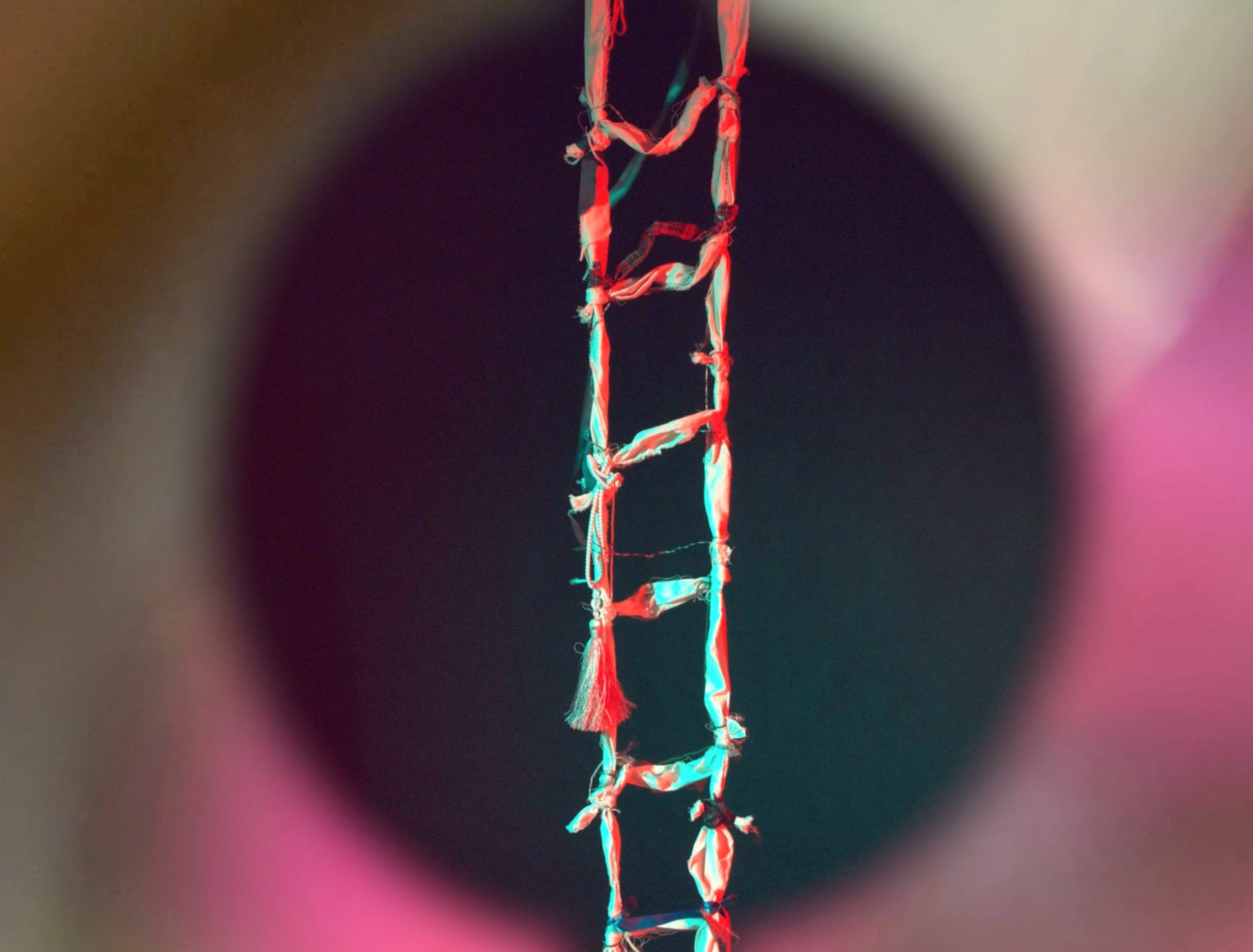 A rope ladder made out of fabric scraps and ribbons hangs in the middle of a dark circle, bright colours fill the background