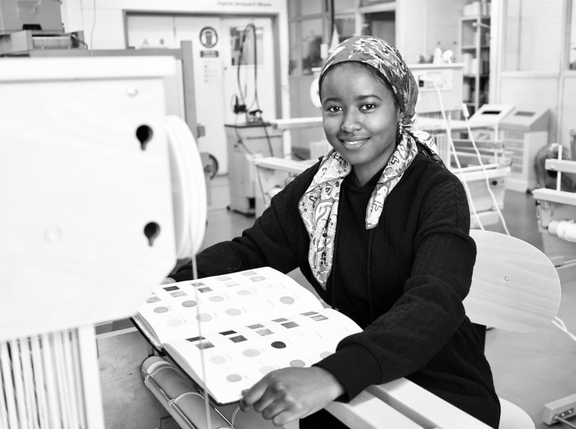 Sauda Imam at the weave studio at Royal College of Art. Imam is sitting in front of a loom with her colourful sketchbook.