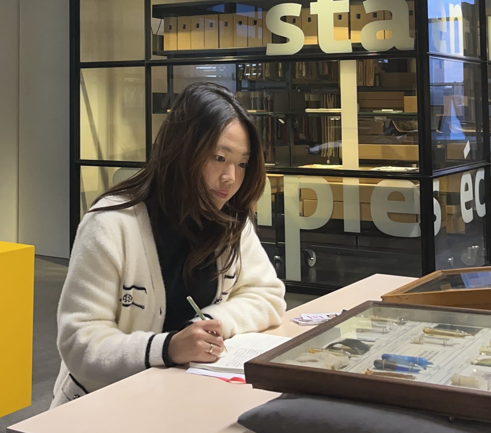 Amber Kim is writing notes while sitting down and examining archives at Textiel Museum.