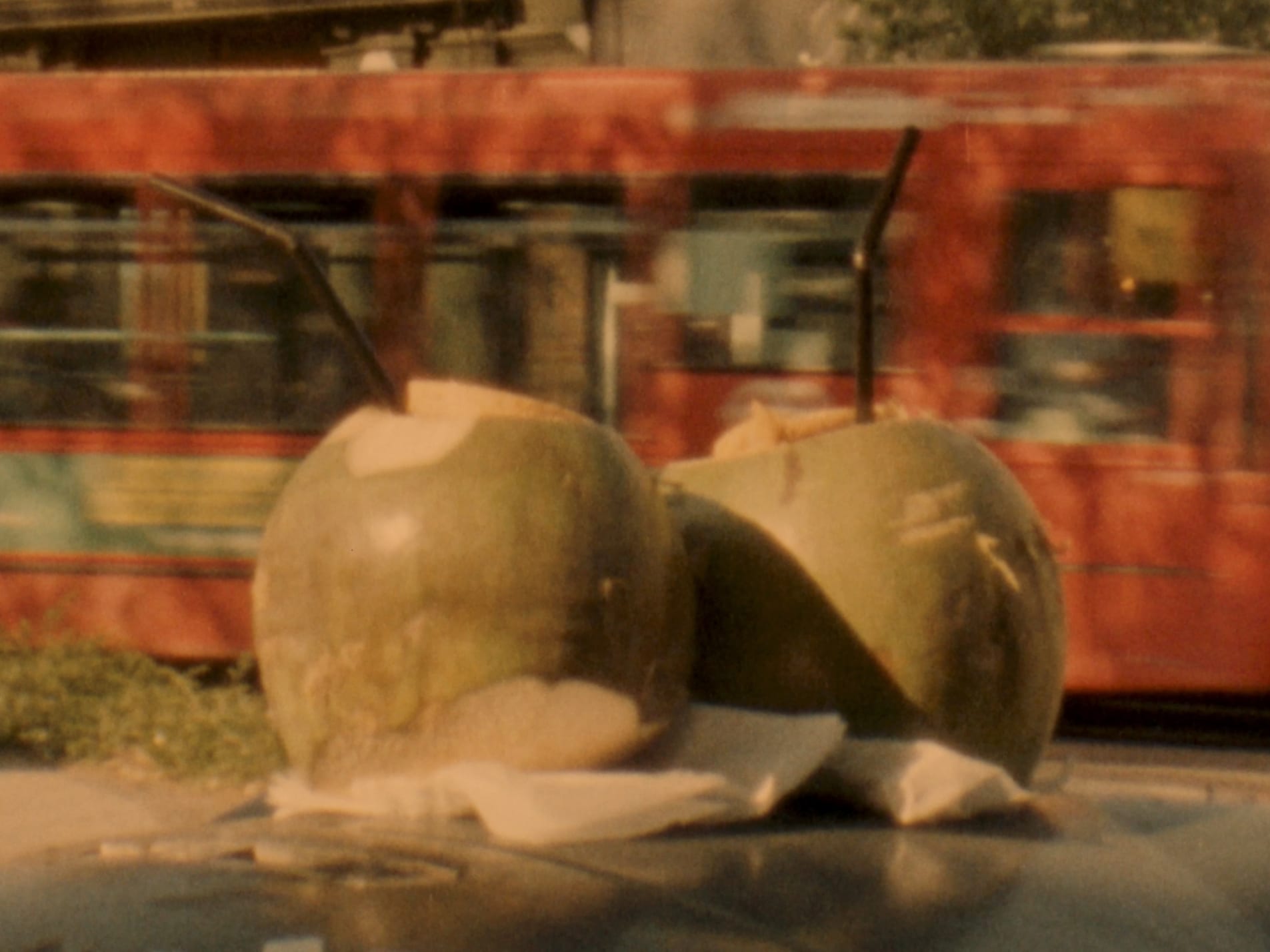 Still of two coconuts with straws on top of a bin with a bus going by in the background shot on super 8