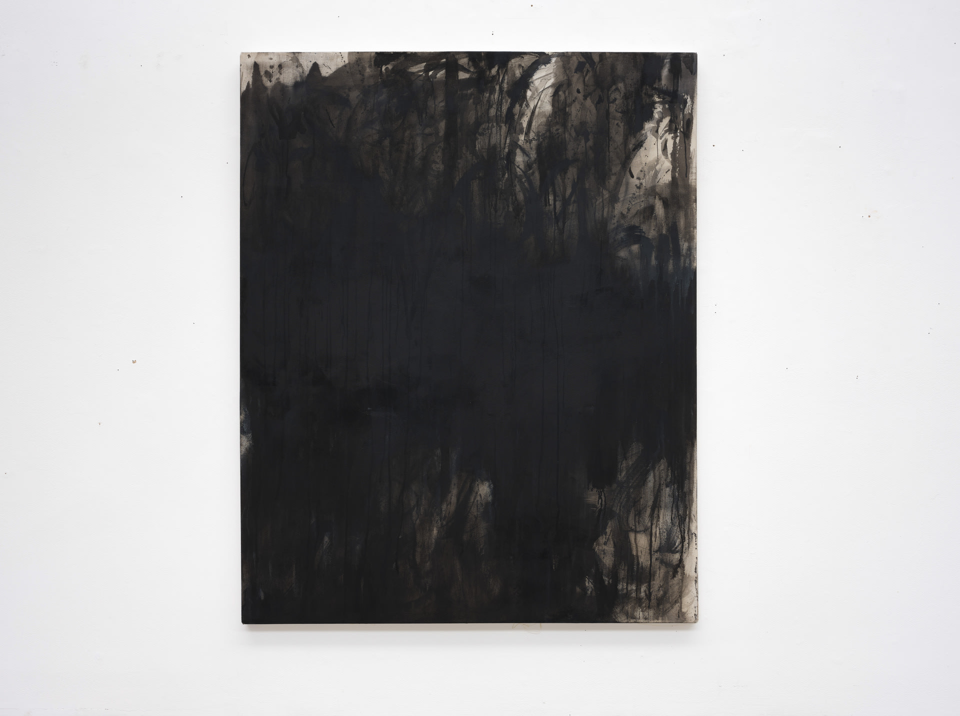 A dark abstract painting hung on a white studio wall. Drips and splatters create a dark forest.