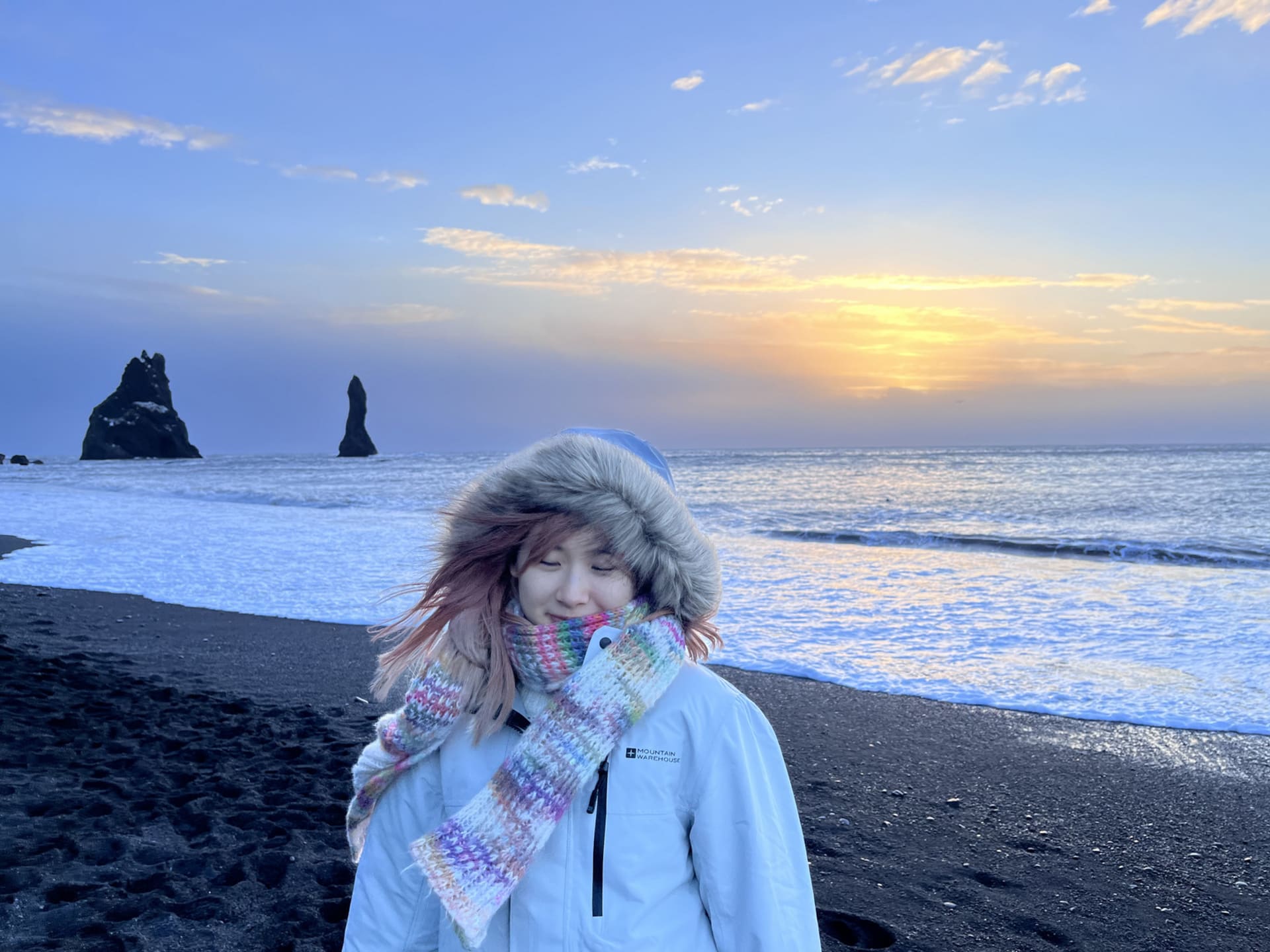 A pink hair girl wearing a white mountain warehouse jacket, standing on the beach.