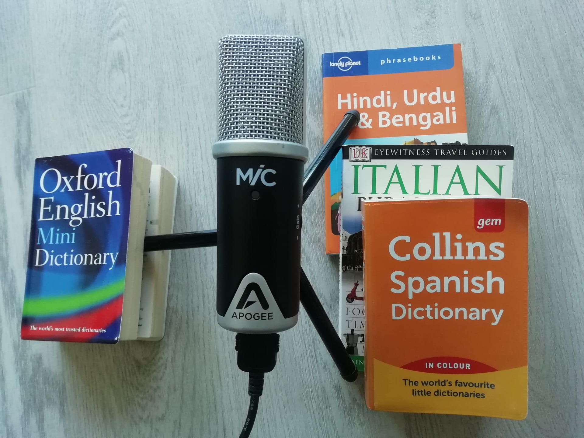 A microphone on a tripod. One leg is on an English dictionary. The other two are on English-Spanish, Italian, Hindi dicionaries.