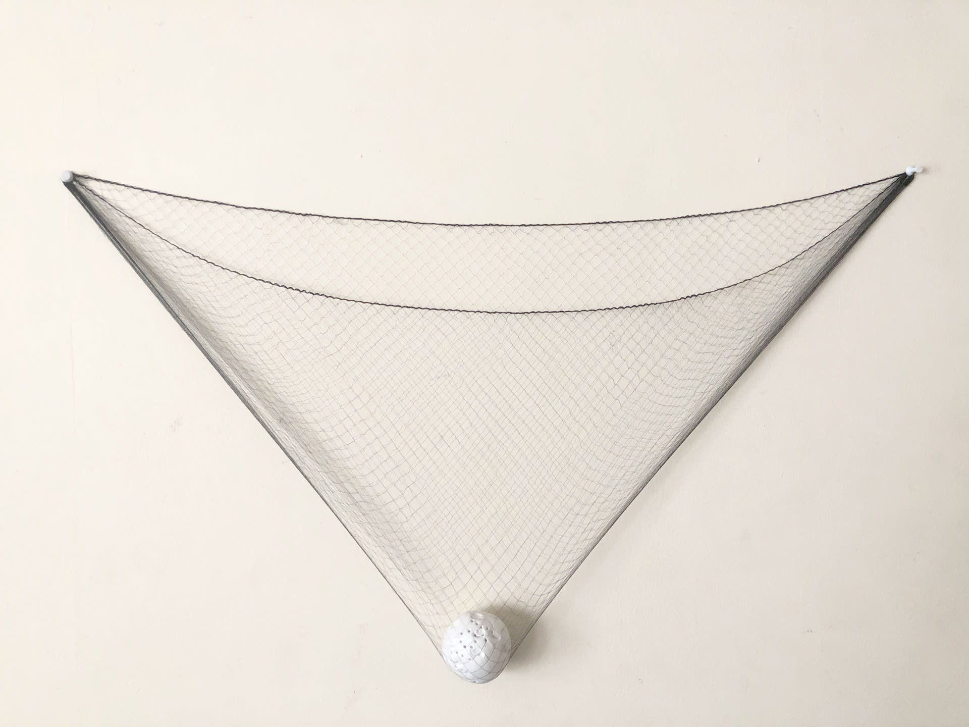 Stretched net held by white plastic pins weighed down into a triangle shape by punctured ball