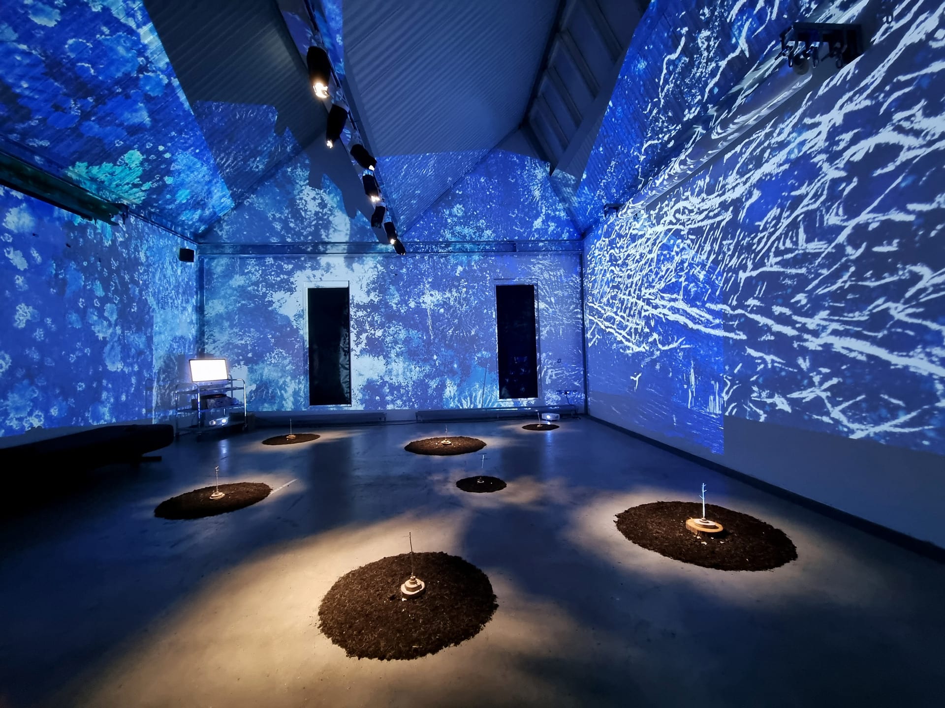 Blue abstract projects cover all walls of a room with circular soil sculptures on floor