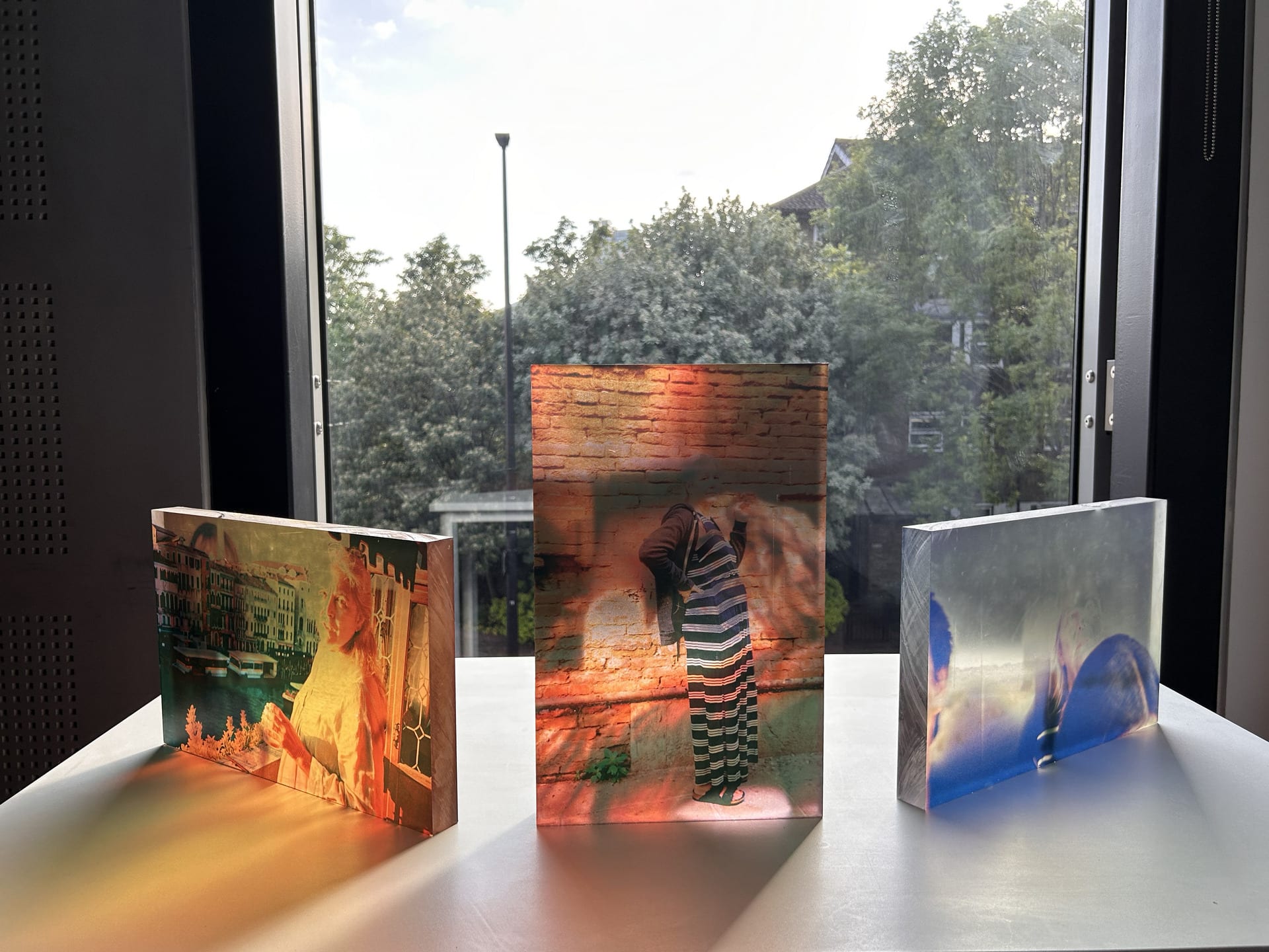 three pieces of acrylic in front of a window with a self portrait of the artist and a picture of her mother on each side