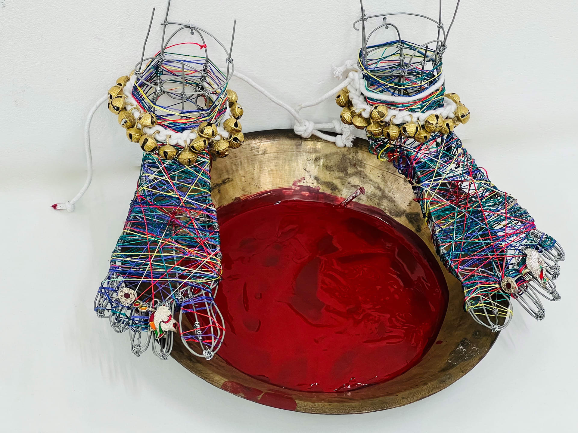 Two feet made of wire, covered with colourful threads and tied together with large bells on a brass plate 