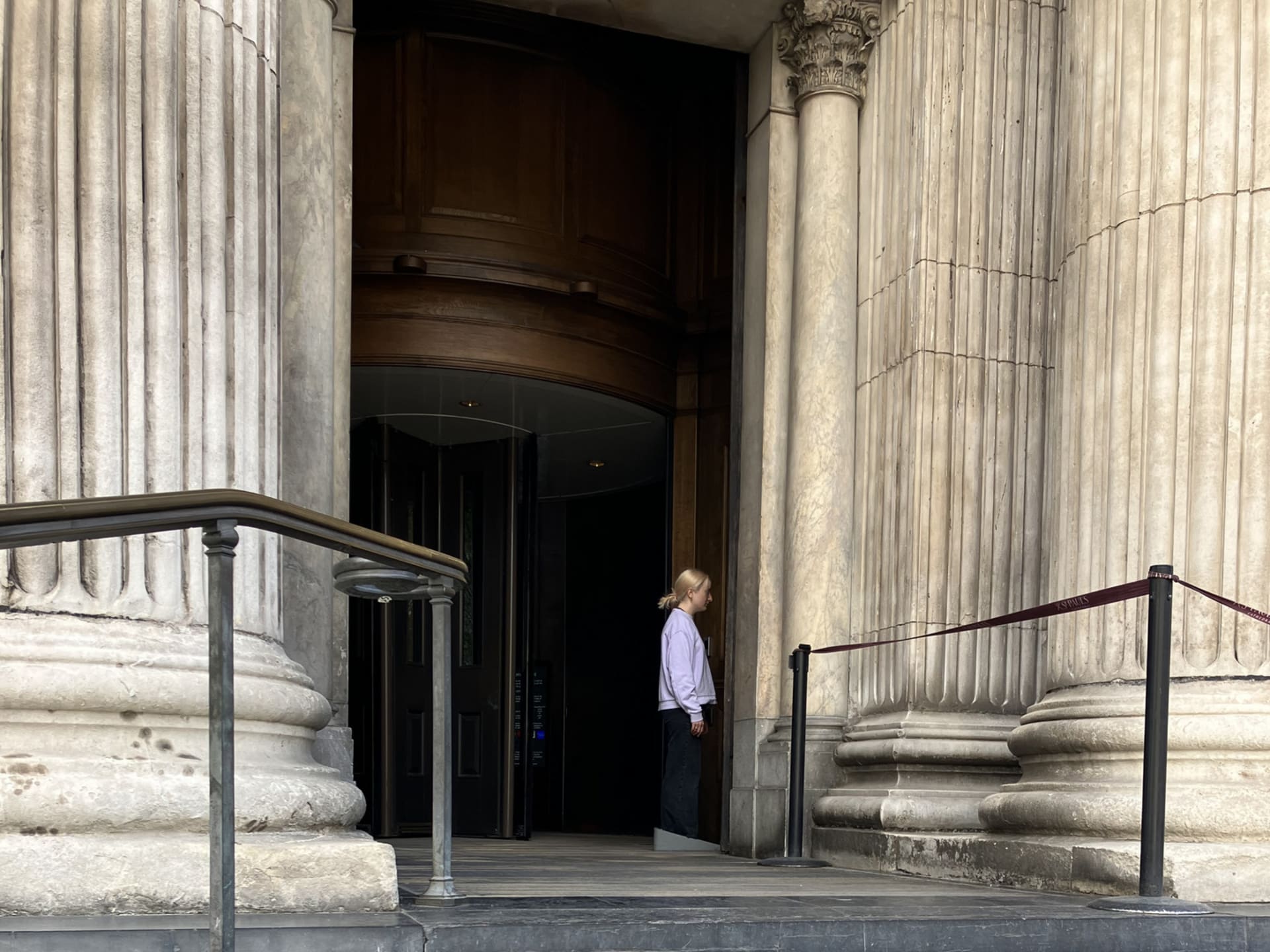 Lili is wearing a large doorstop shaped grey rubber show and is holding the door open with it at st. pauls cathedral