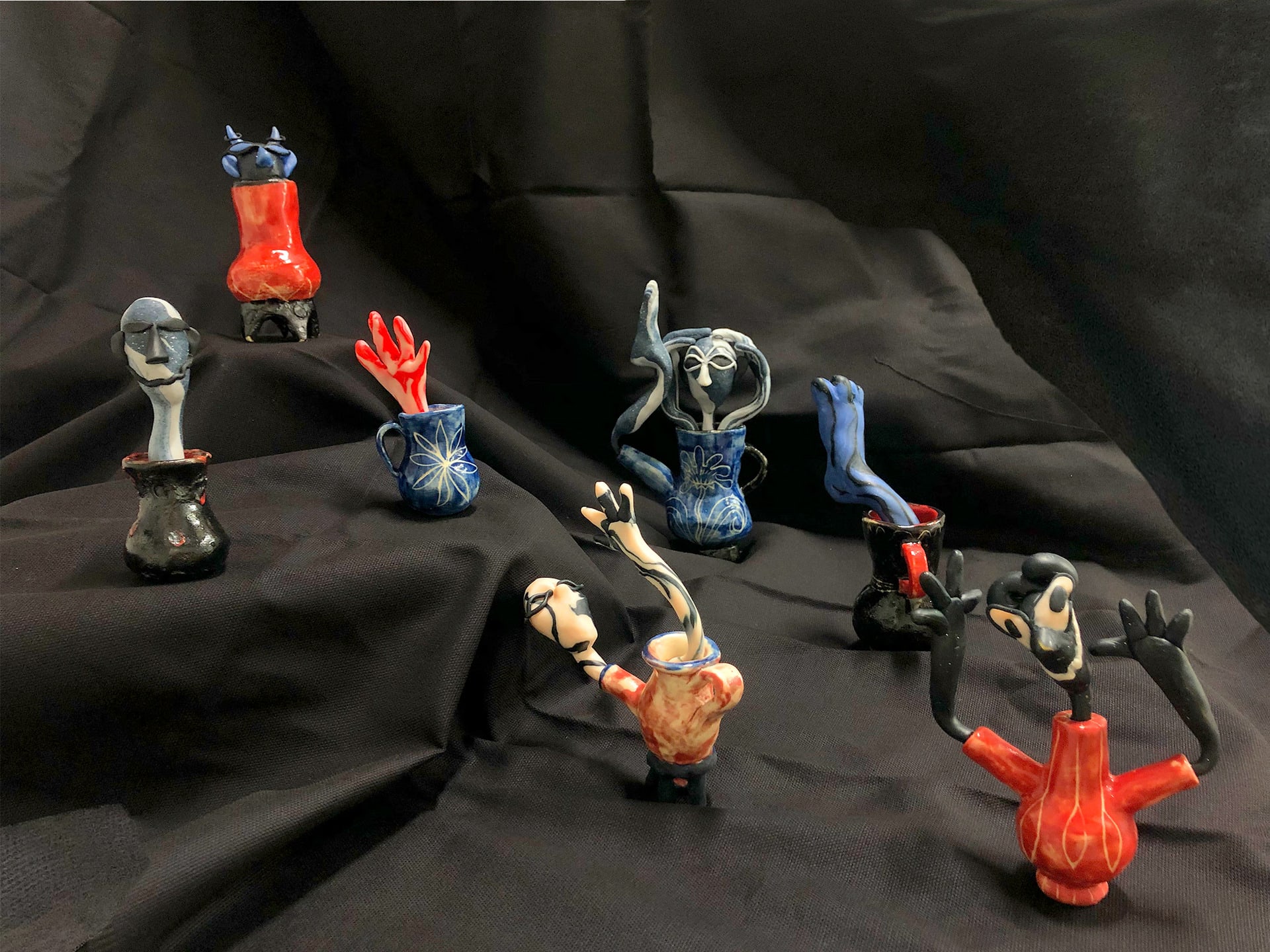 7 miniature ceramic vessels from which colourful polymer clay entities stick ou