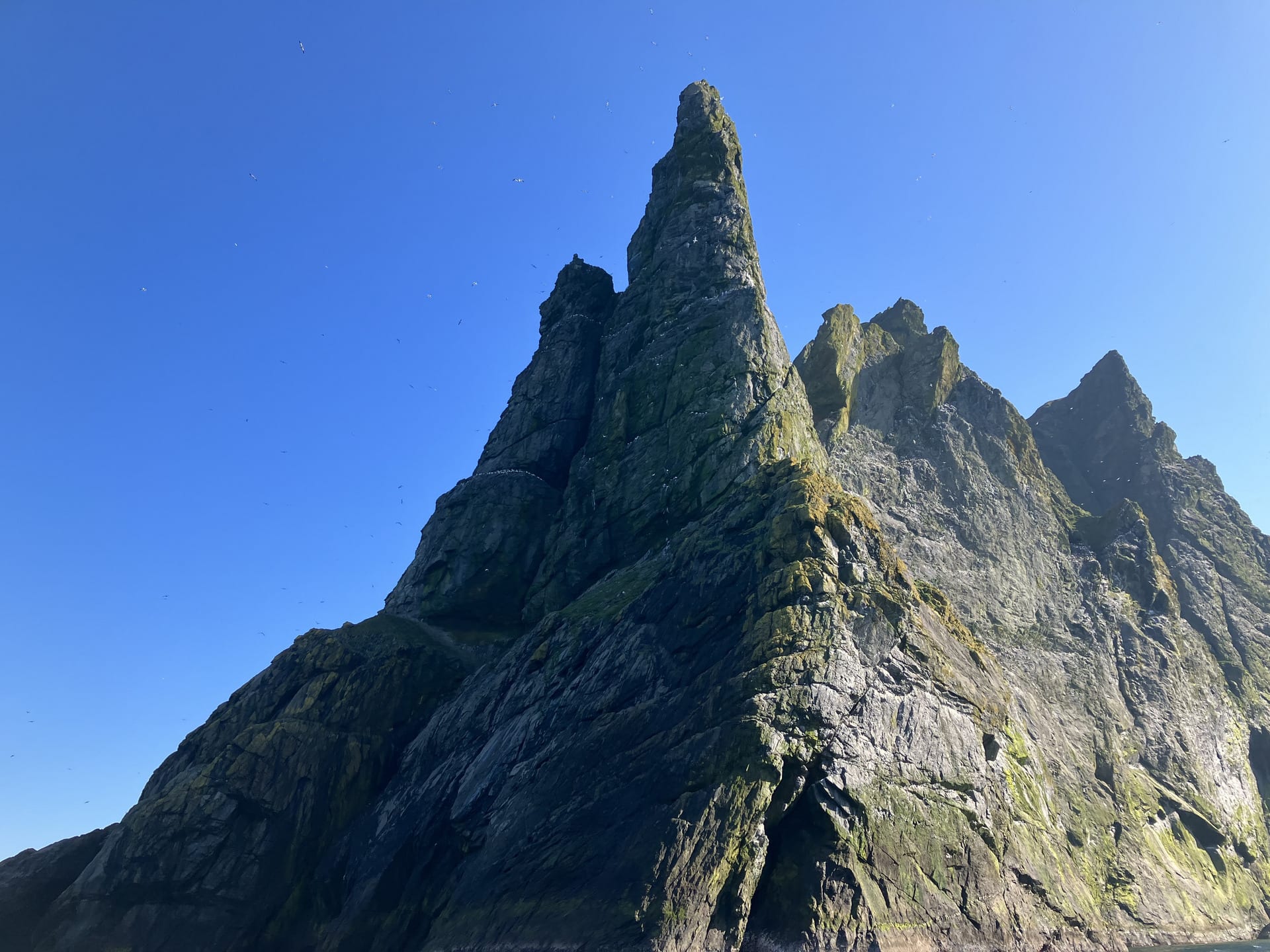 Sharp pointed rocks of grey and green zigzag across the blue sky. The sea is below them.