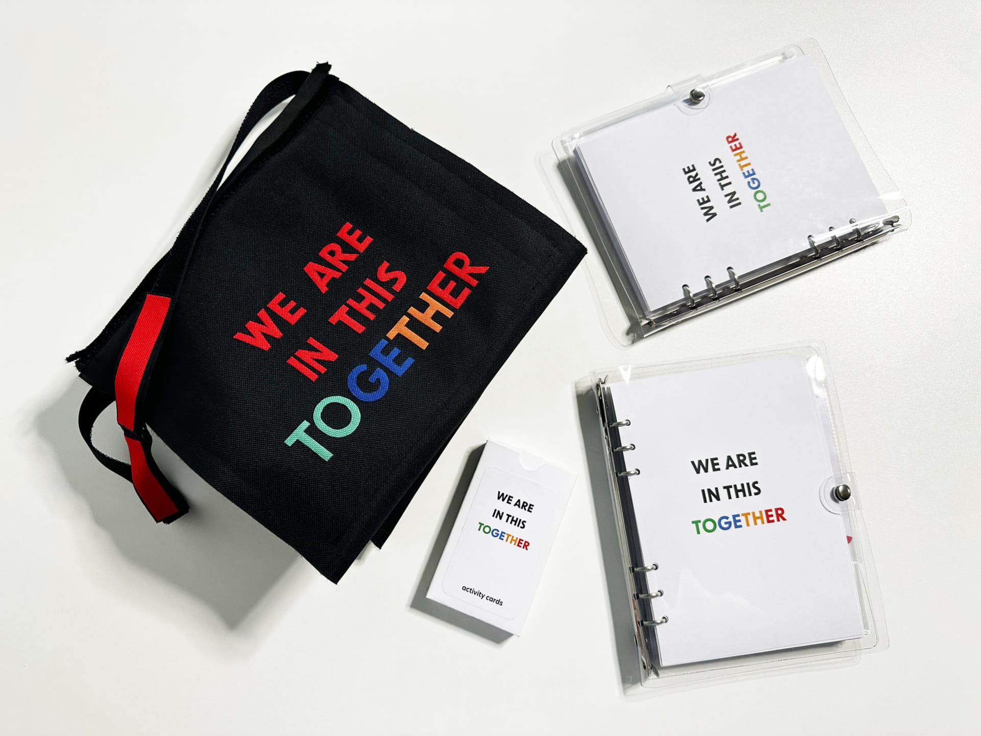 A black fabric bag, a box of activity cards, and 2 copies of the workbook. ‘We are in this together’ is written on all of them