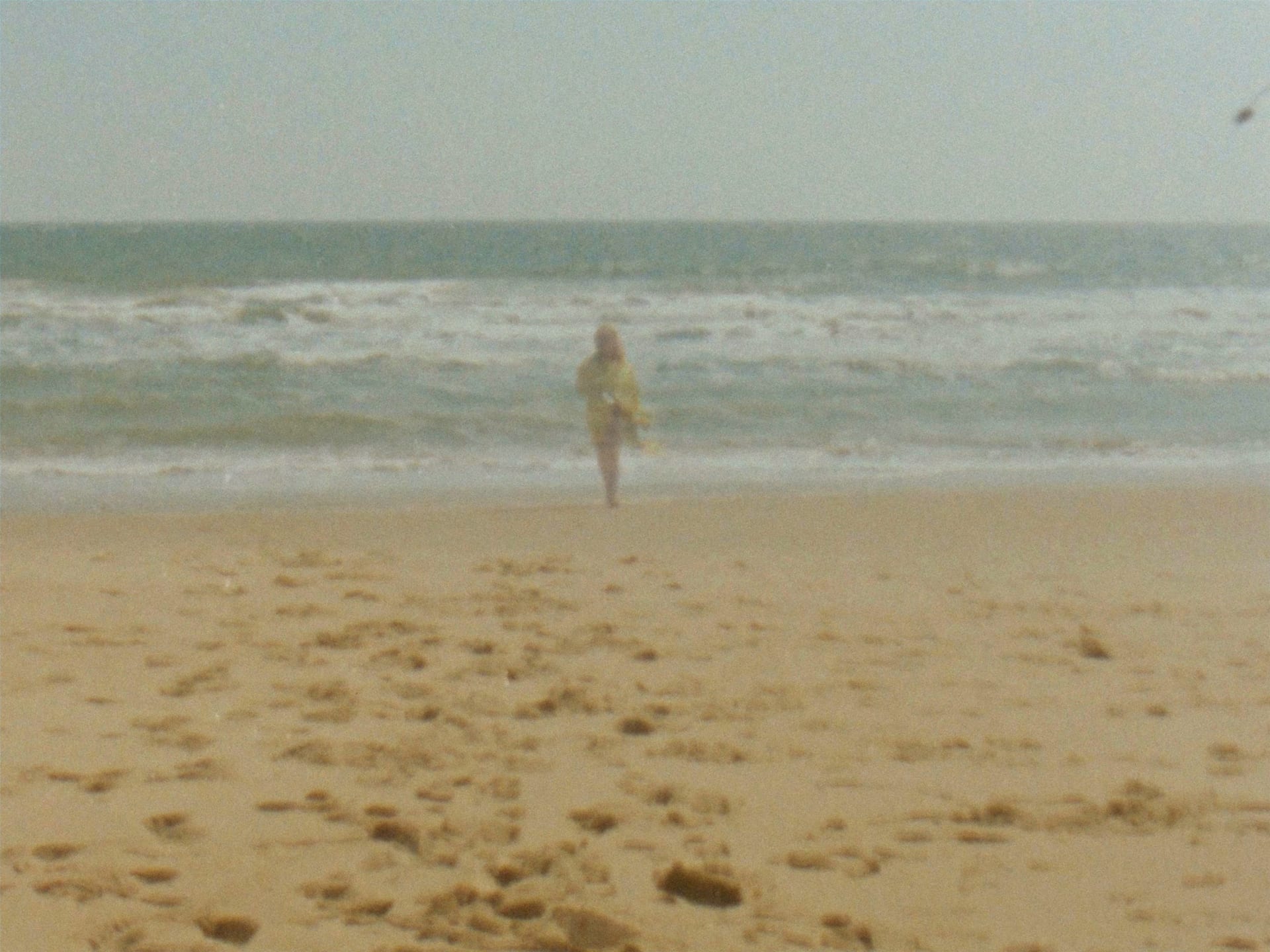 Still of super 8 film where we see the artist emerging from the sea, wearing a foil blanket