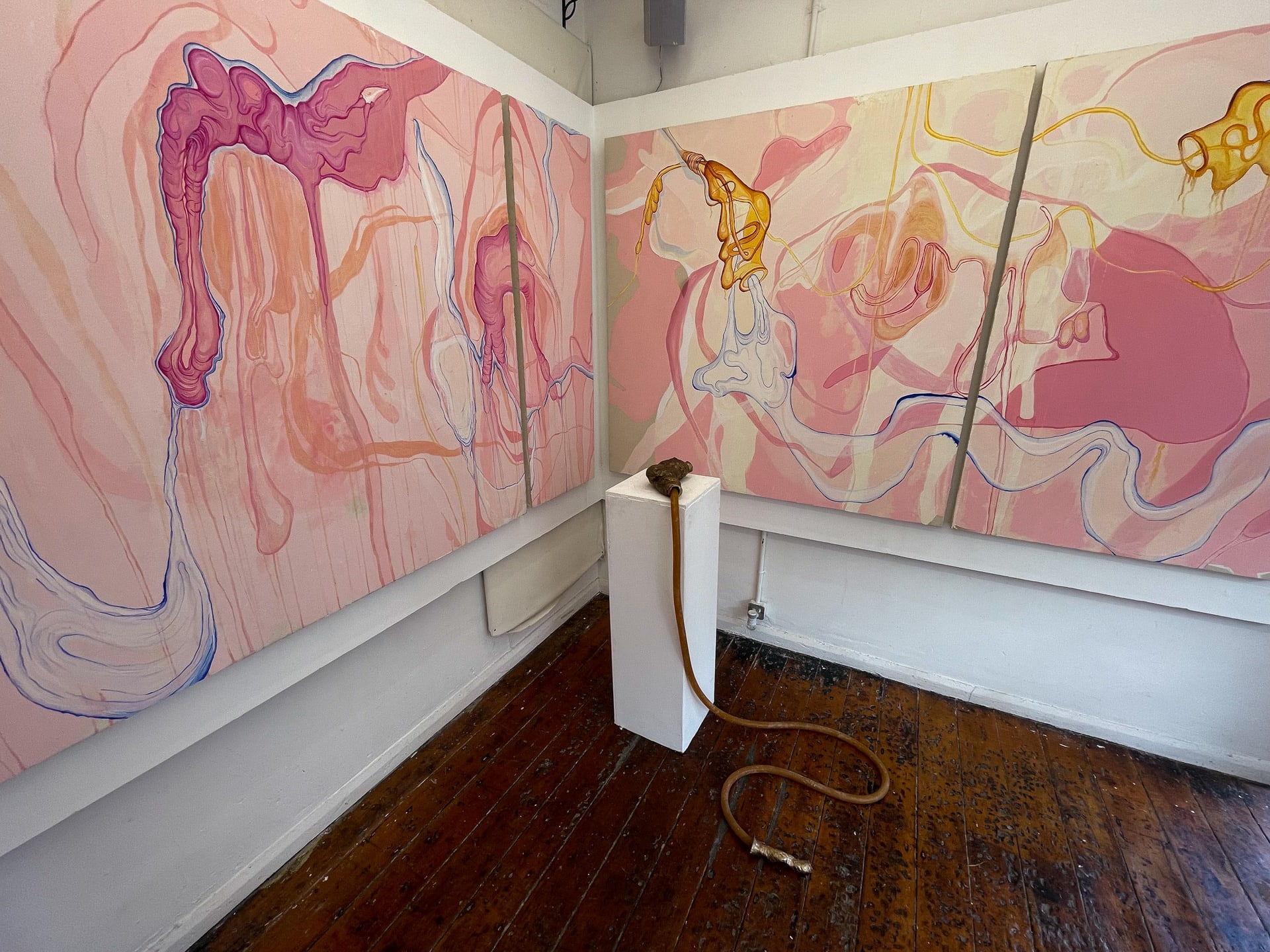 Wide perspective of two large pink paintings intersecting at corner and meeting with bronze sculpture