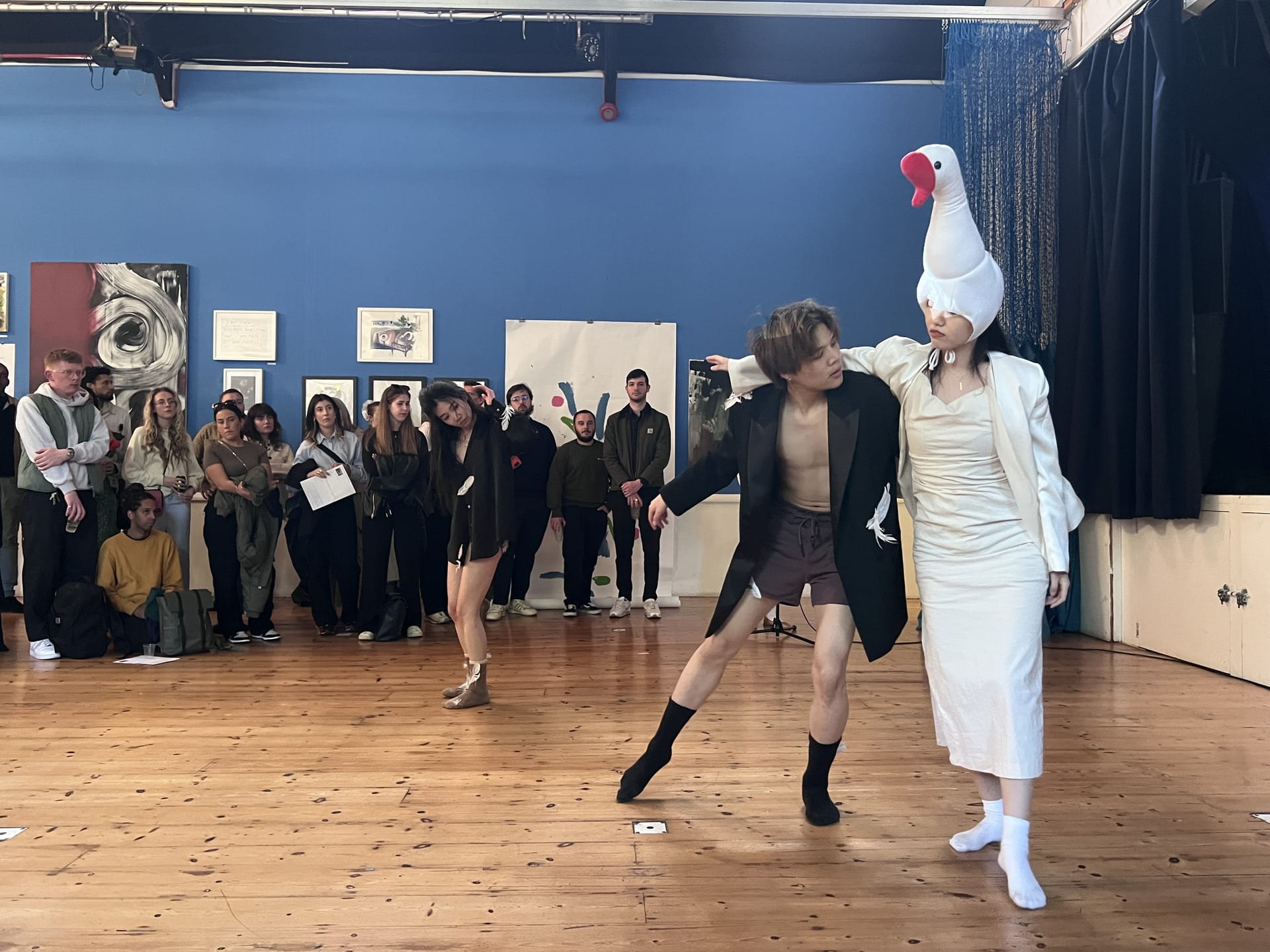 A photo of a performance with three actors dressed in costume dancing whilst spectators watch.