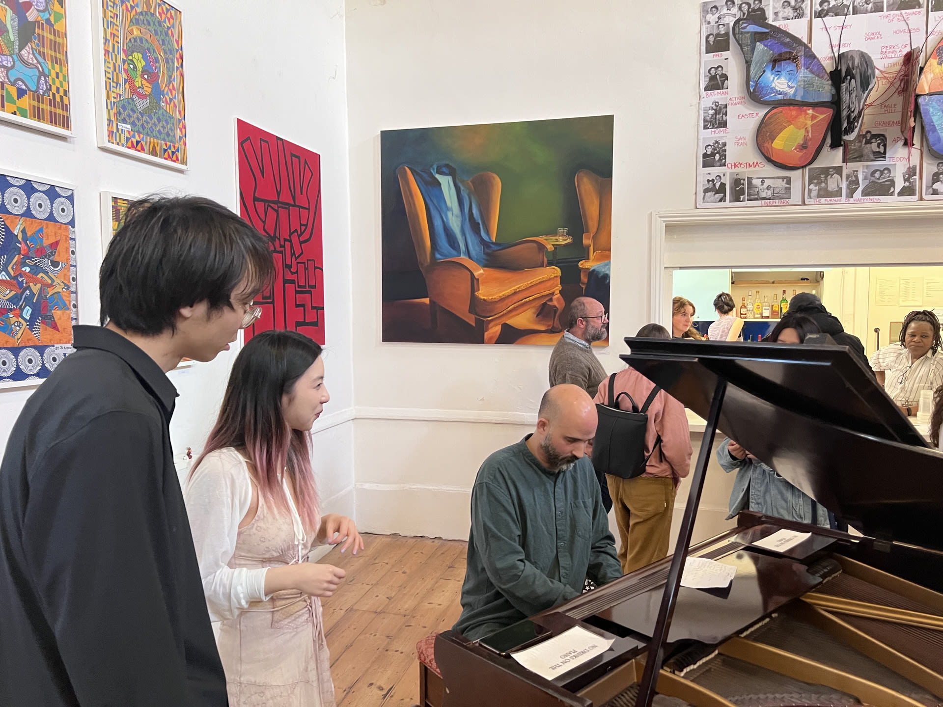 A pianist playing the piano for the performance whilst spectators stand and watch surrounded by paintings.