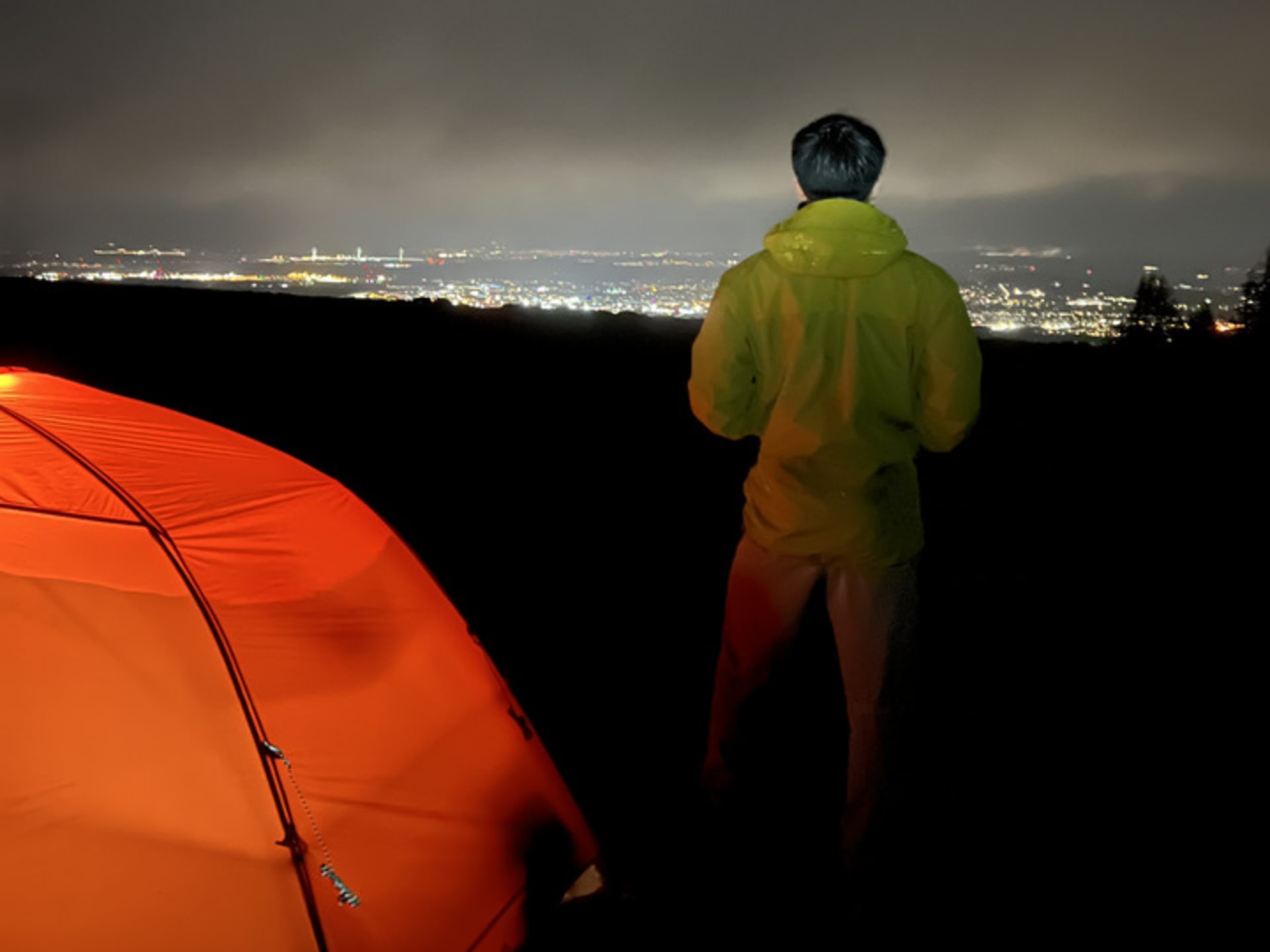 A man standing by his tent at night.