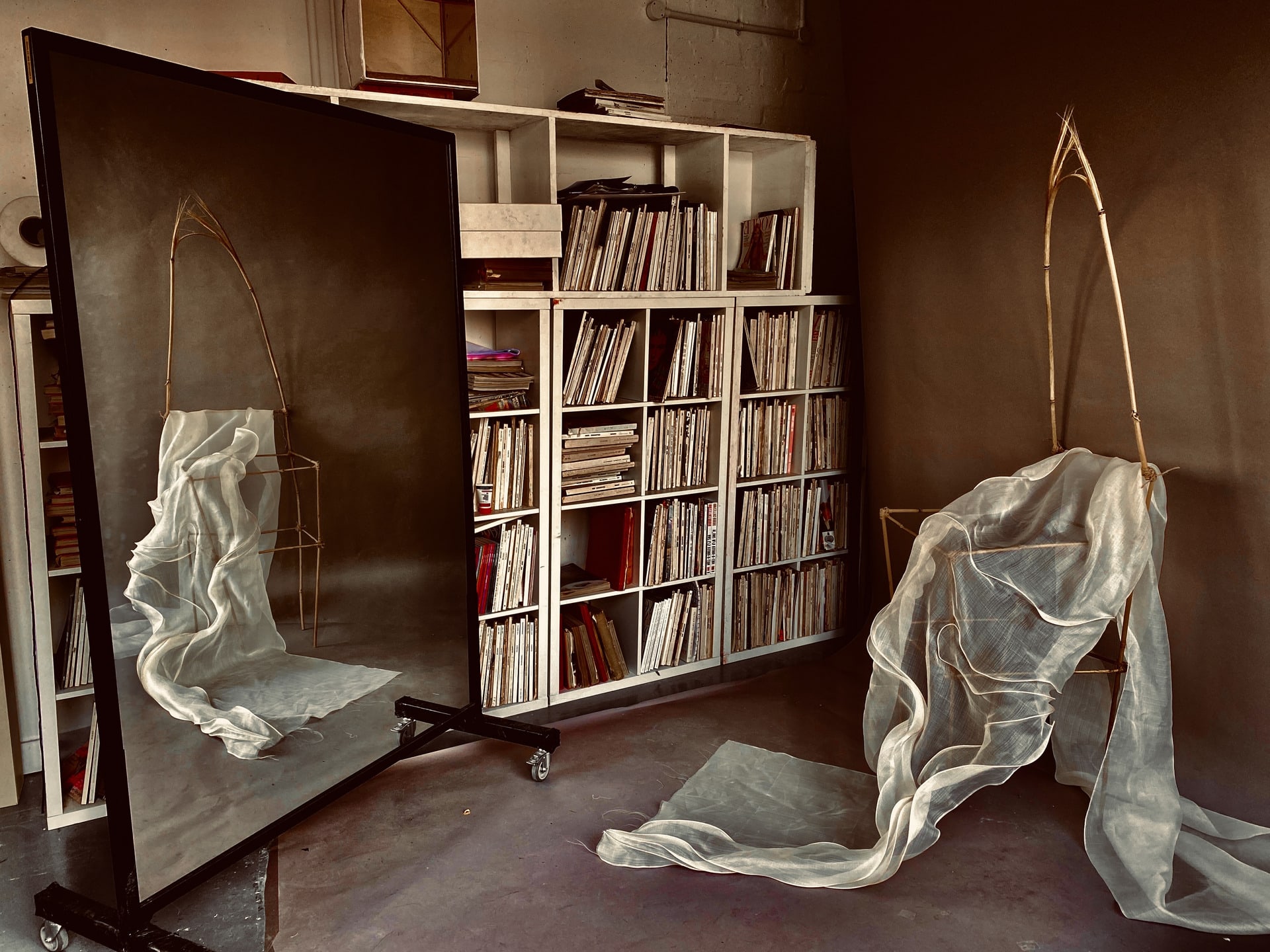 Bamboo chair sculpture with piña fabric running through the chair in front of a mirror.